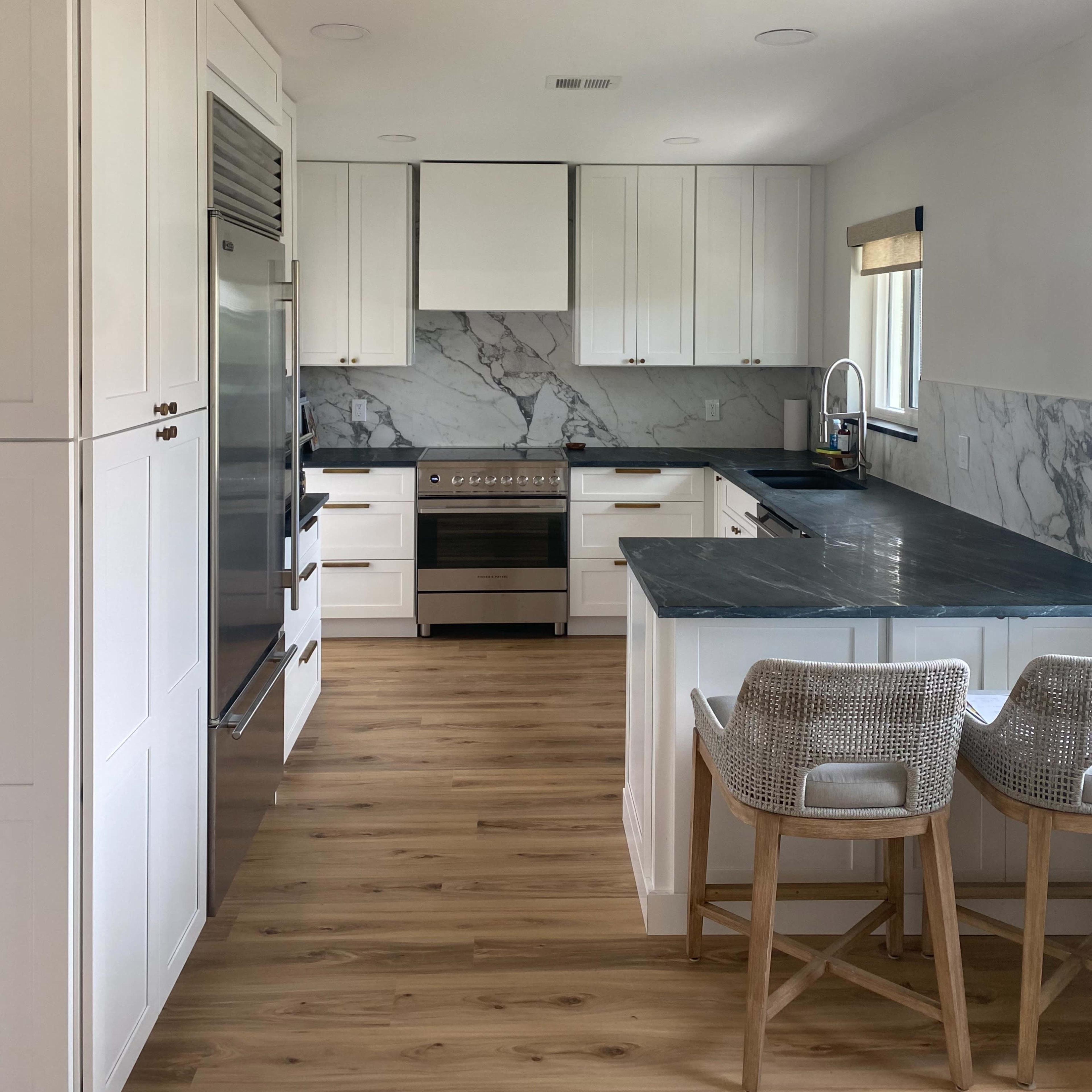 A modern kitchen features white cabinets, a marble backsplash, stainless steel appliances, and a wooden floor.