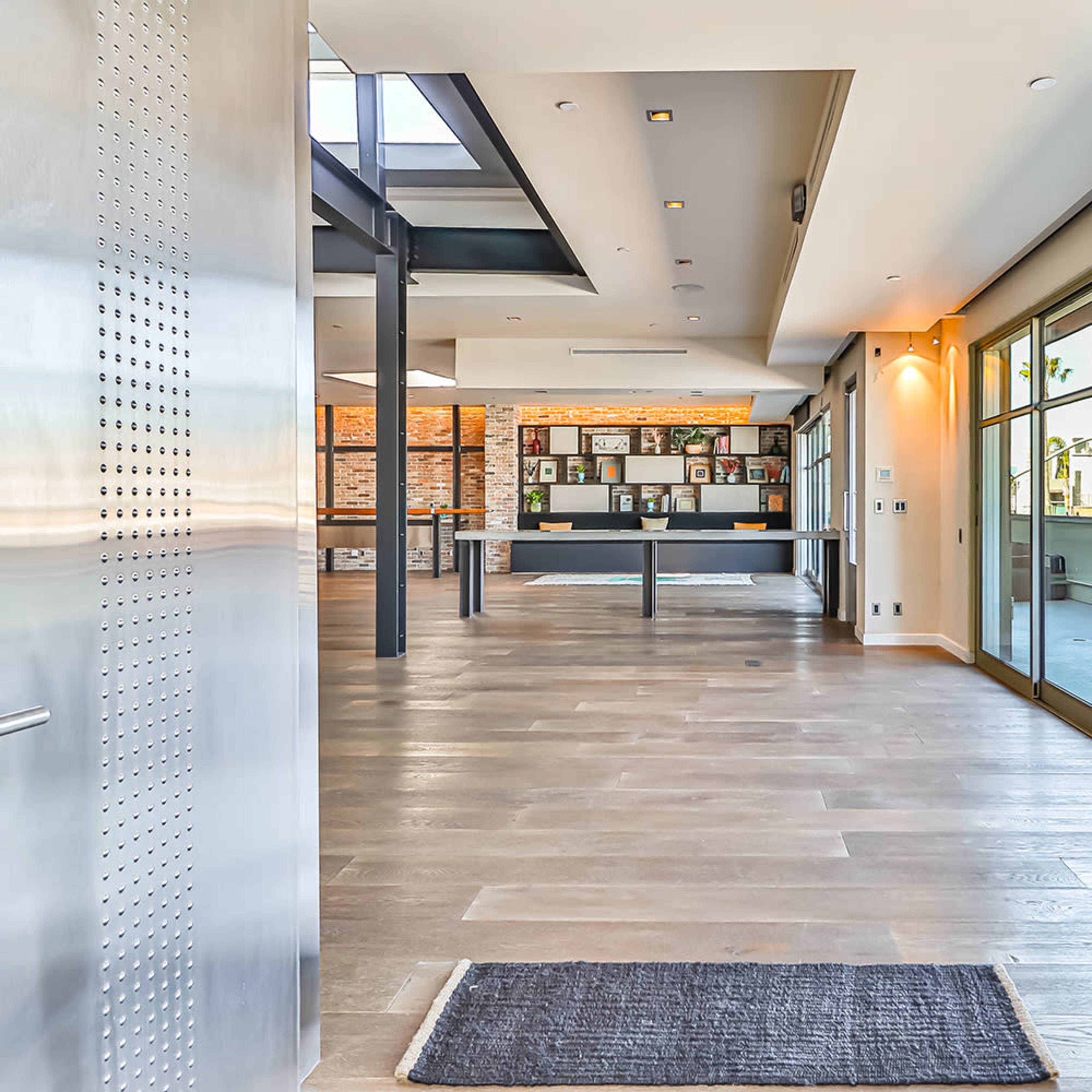 A modern entryway with large stainless steel doors leading into a bright, open interior space featuring wooden flooring and a gallery area with framed photos.