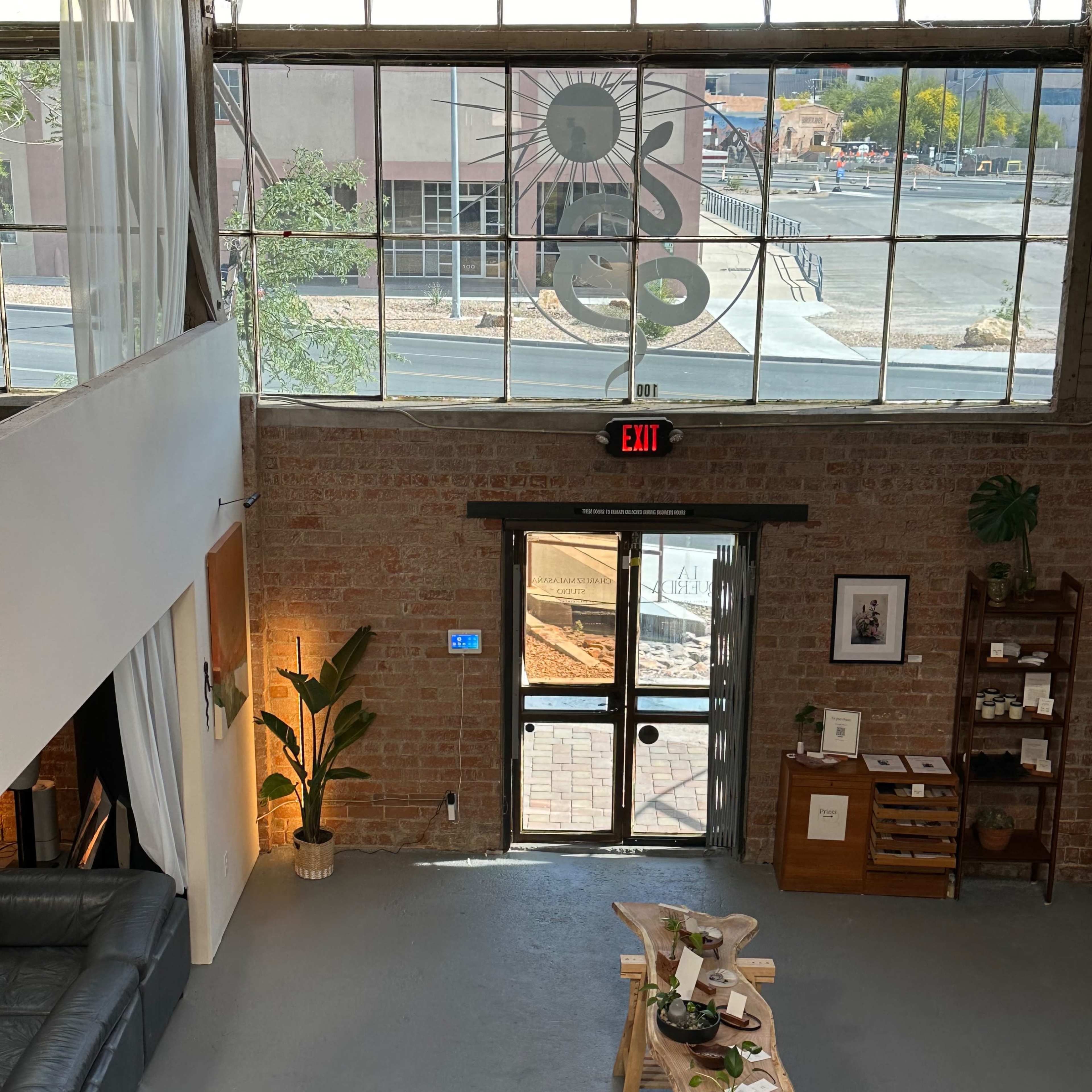 A modern interior of a space with large windows, a seating area, and a table displaying plants, leading to an exit door.