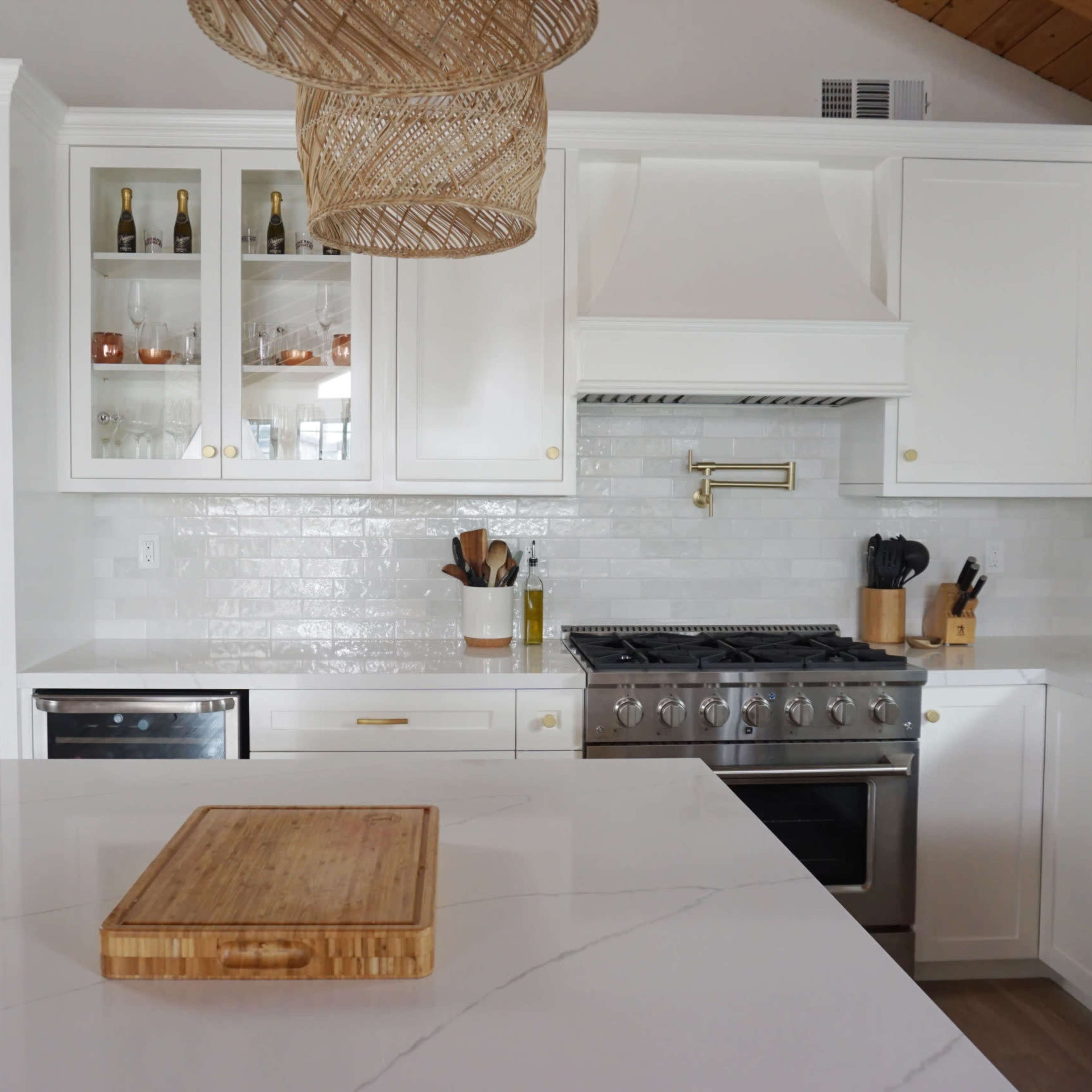 A modern kitchen features white cabinetry, a large marble island with a wooden cutting board, and stainless steel appliances.
