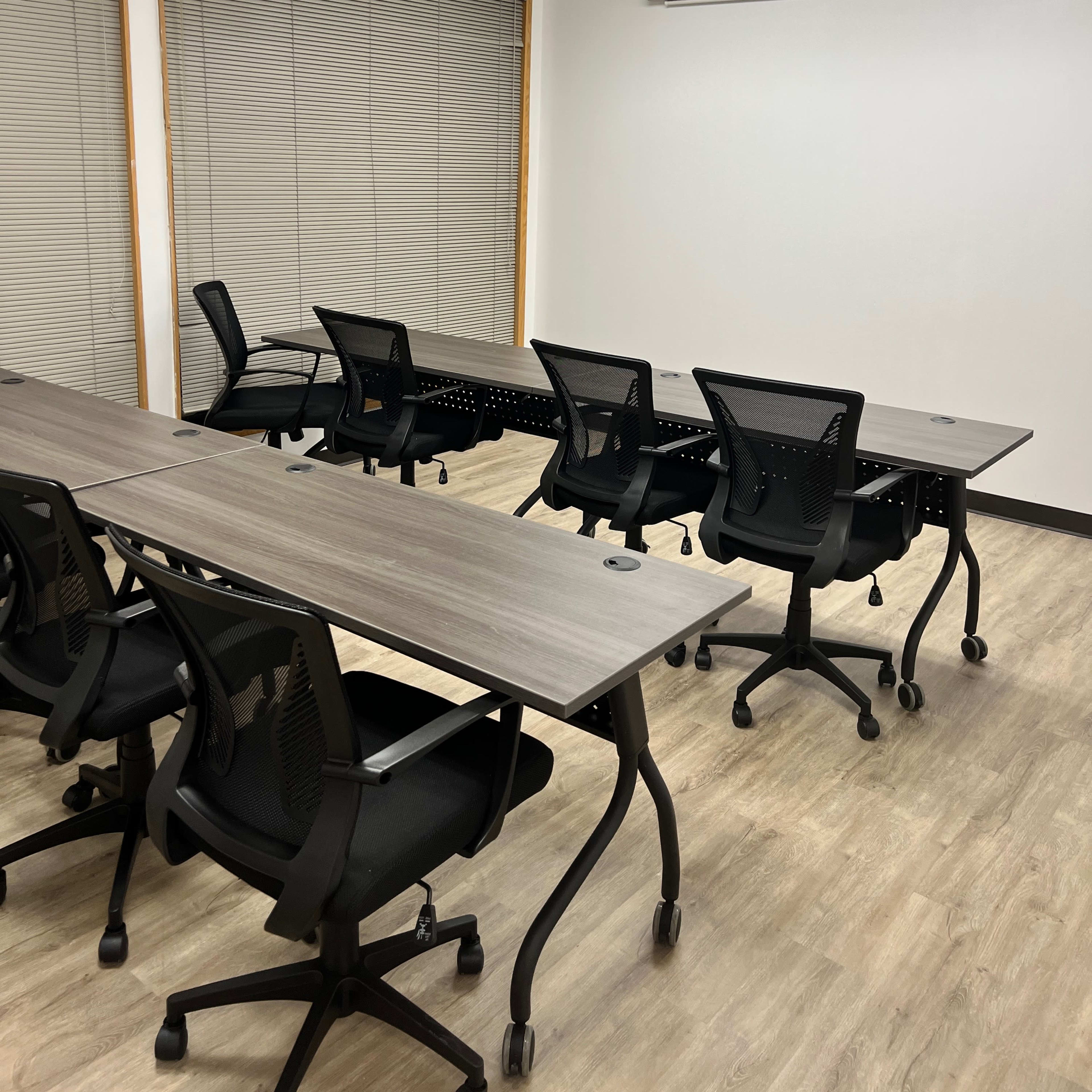 A modern conference room features several mobile desks and chairs arranged around a screen and projector.