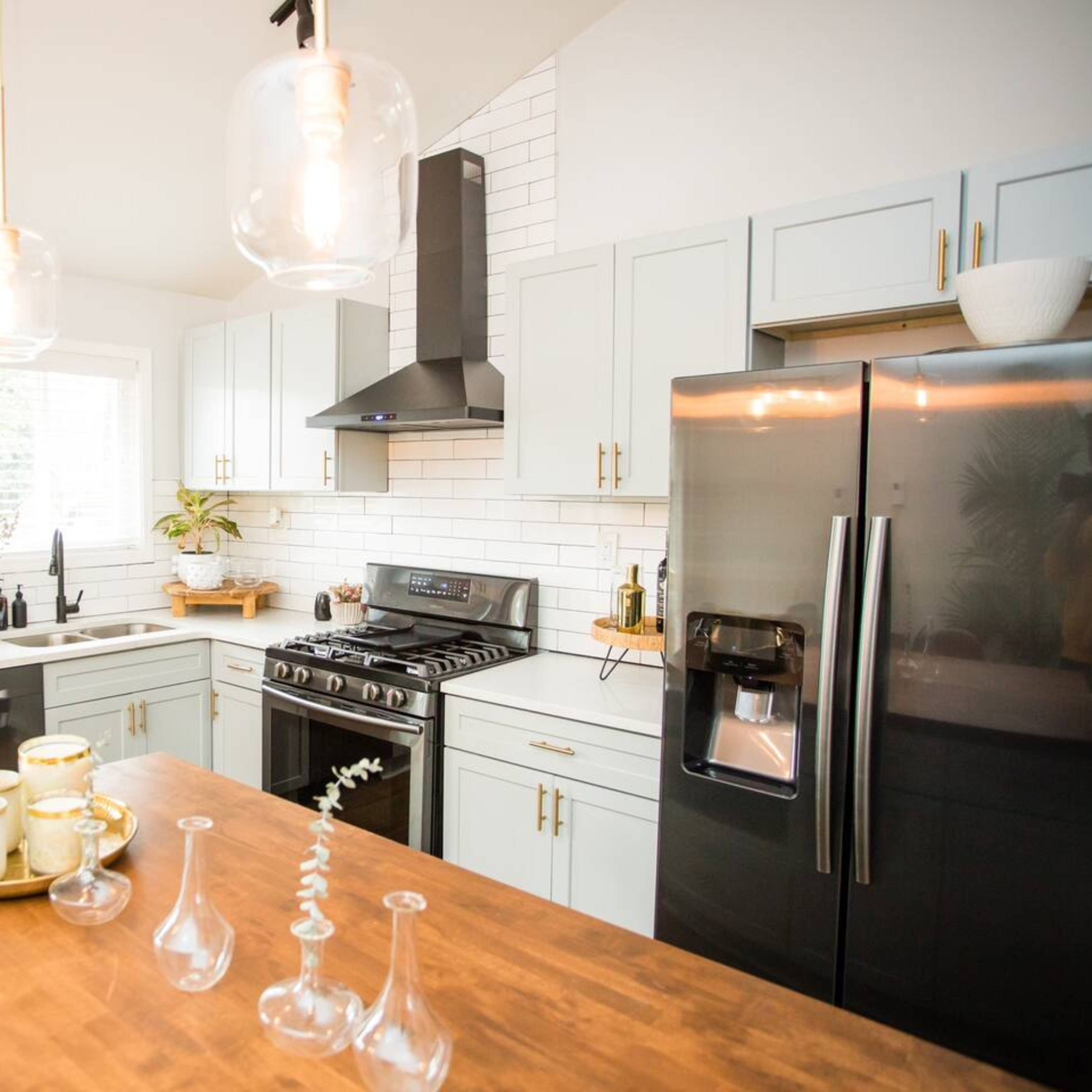 A modern kitchen with light blue cabinets, a black refrigerator, a gas stove, and a wooden dining table with decorative items.