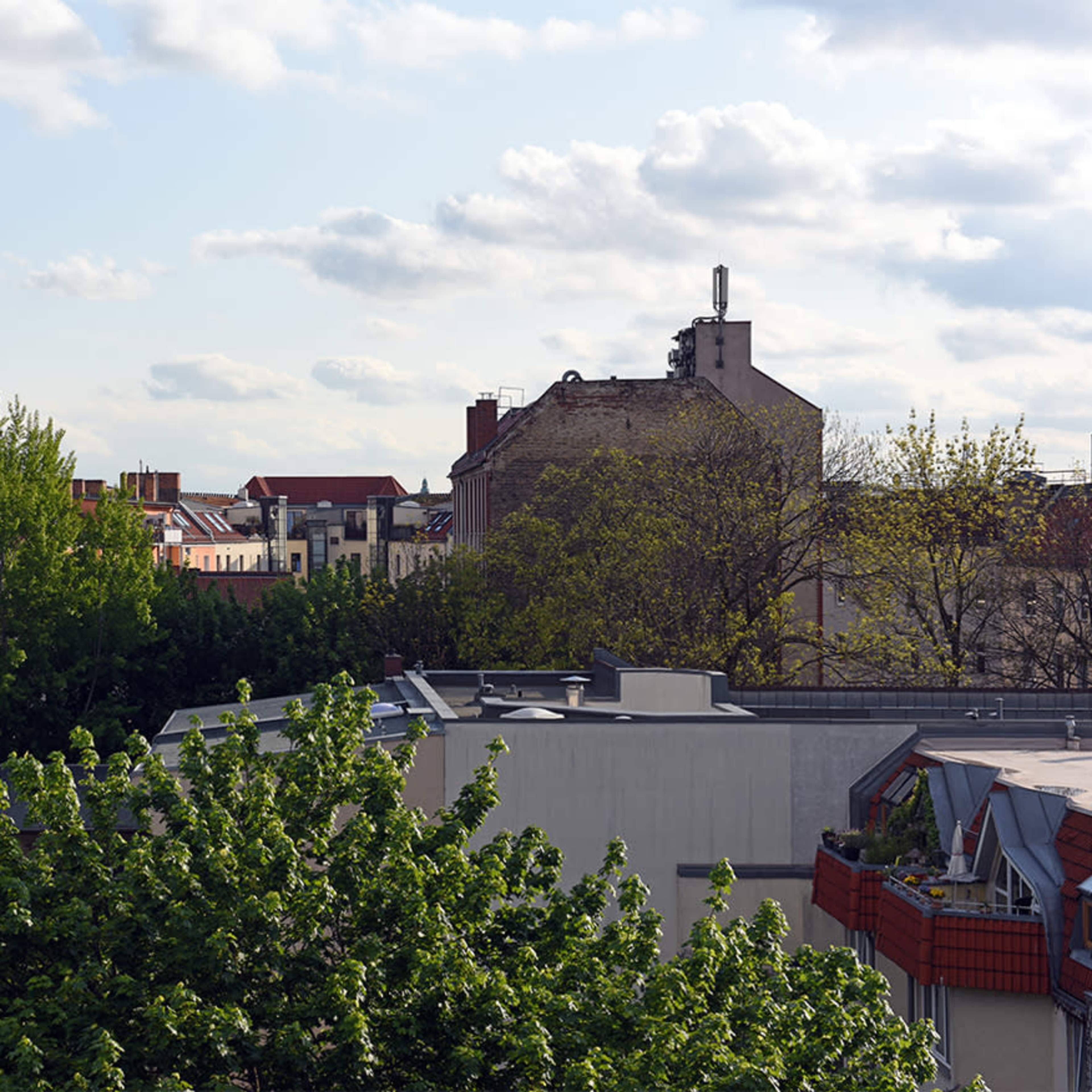 A cityscape with rooftops, trees, and a distant tower visible under a partly cloudy sky.