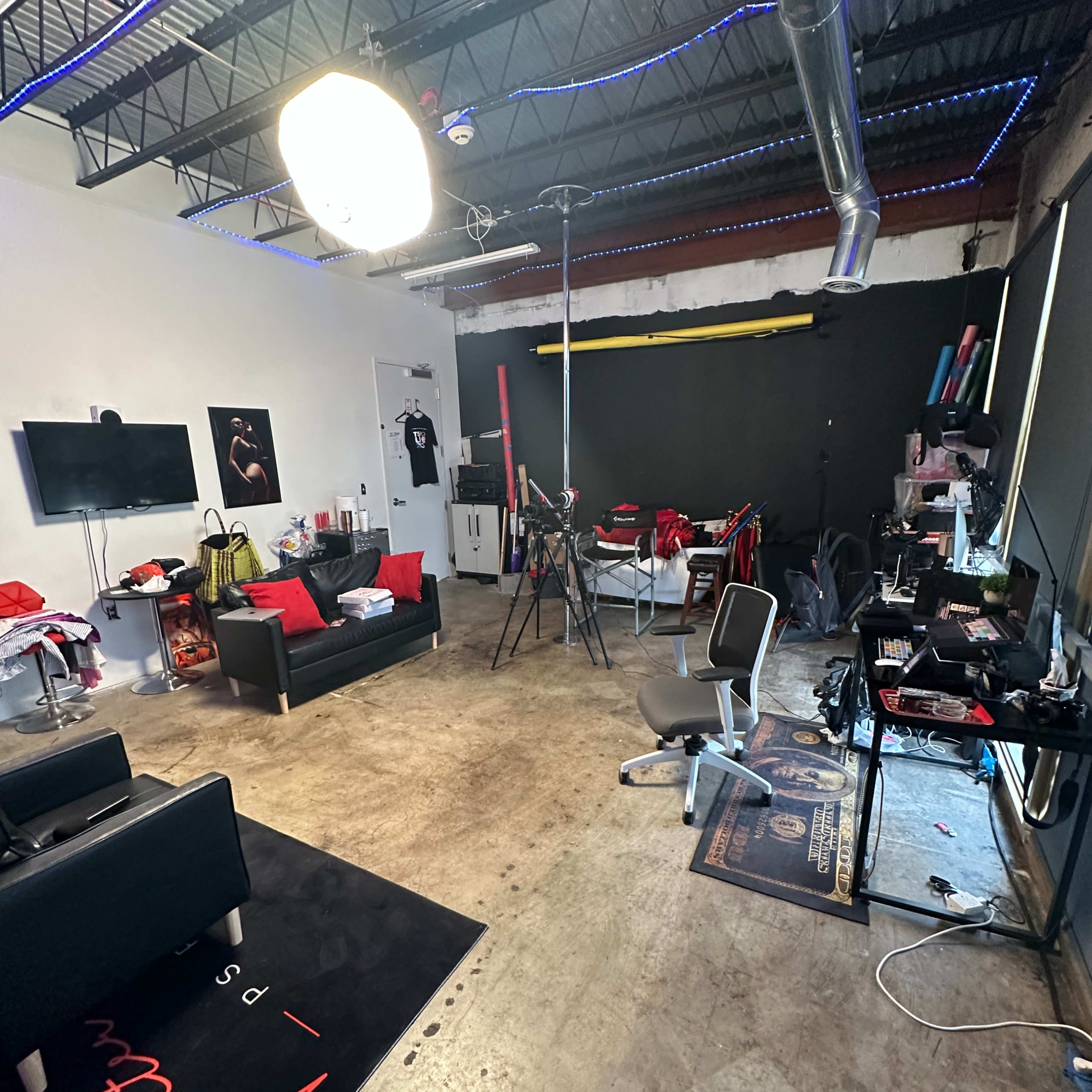 A well-lit studio space with a seating area, a television, various photography equipment, and a cluttered floor.