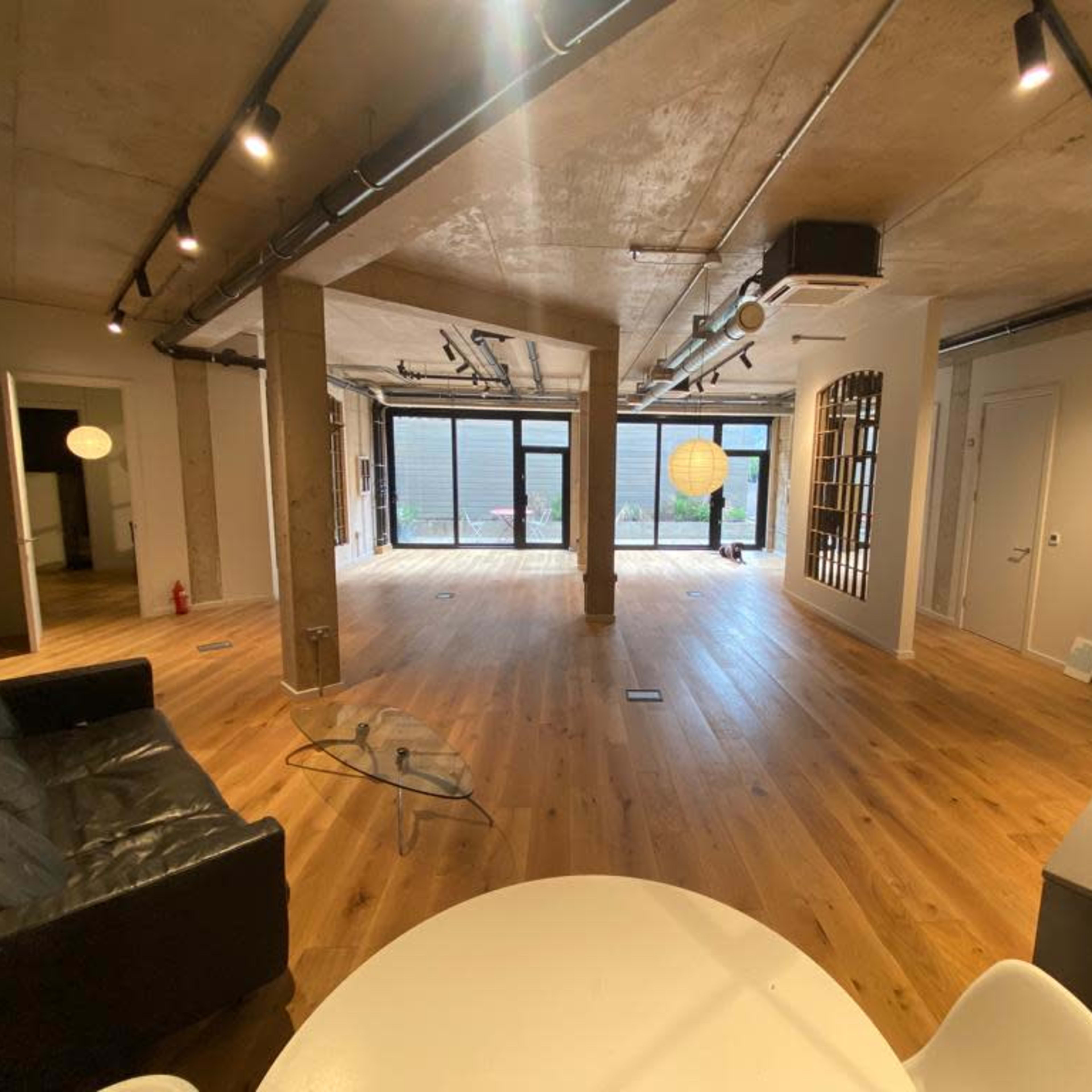 A spacious, modern interior of a room with wooden flooring, large windows, and various sections defined by walls and furniture.