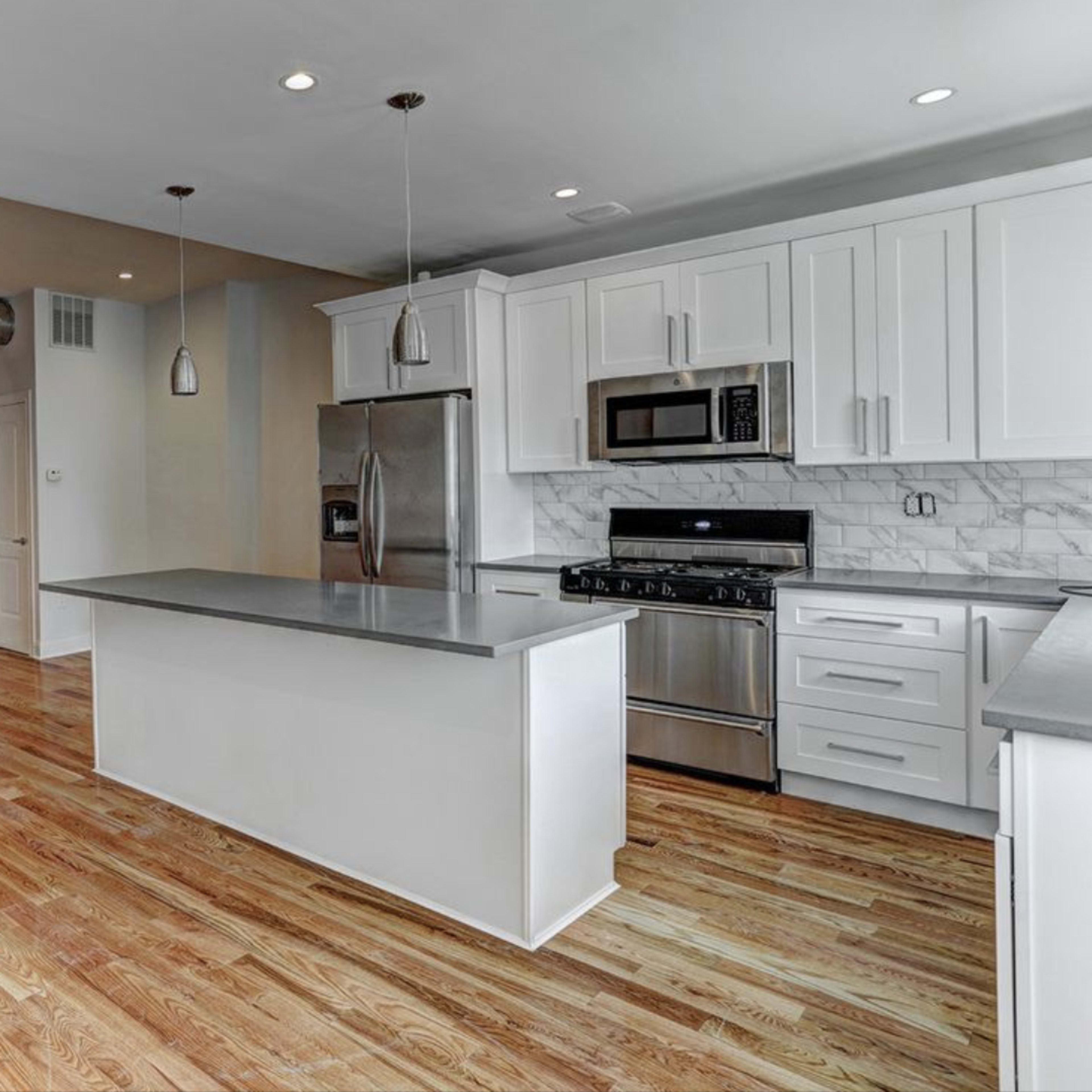 An open-concept kitchen and living area with hardwood floors, modern appliances, and an island in the center.