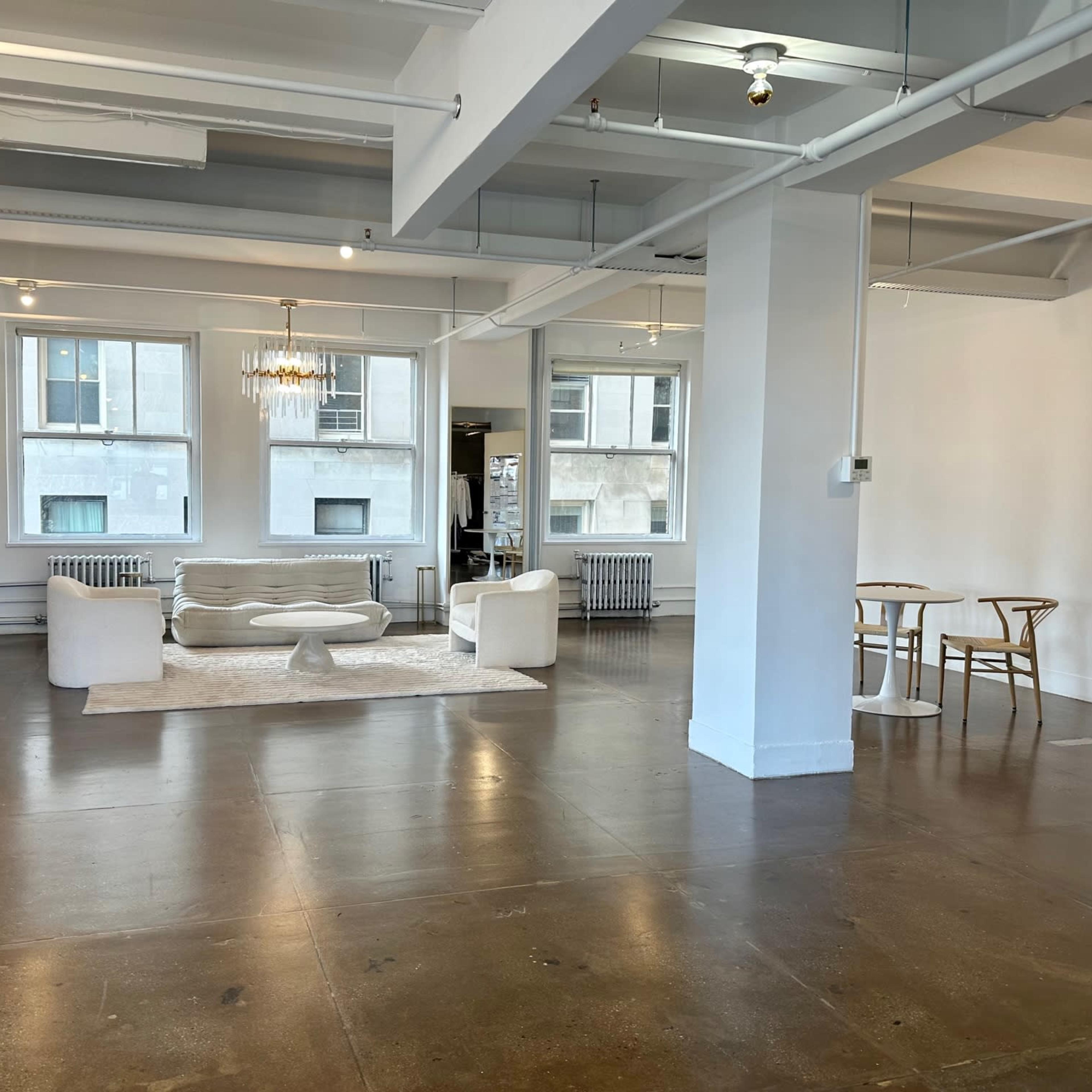 A spacious, minimalist interior with white walls, polished concrete floors, a seating area with a light-colored sofa, a coffee table, and a small dining table with chairs.
