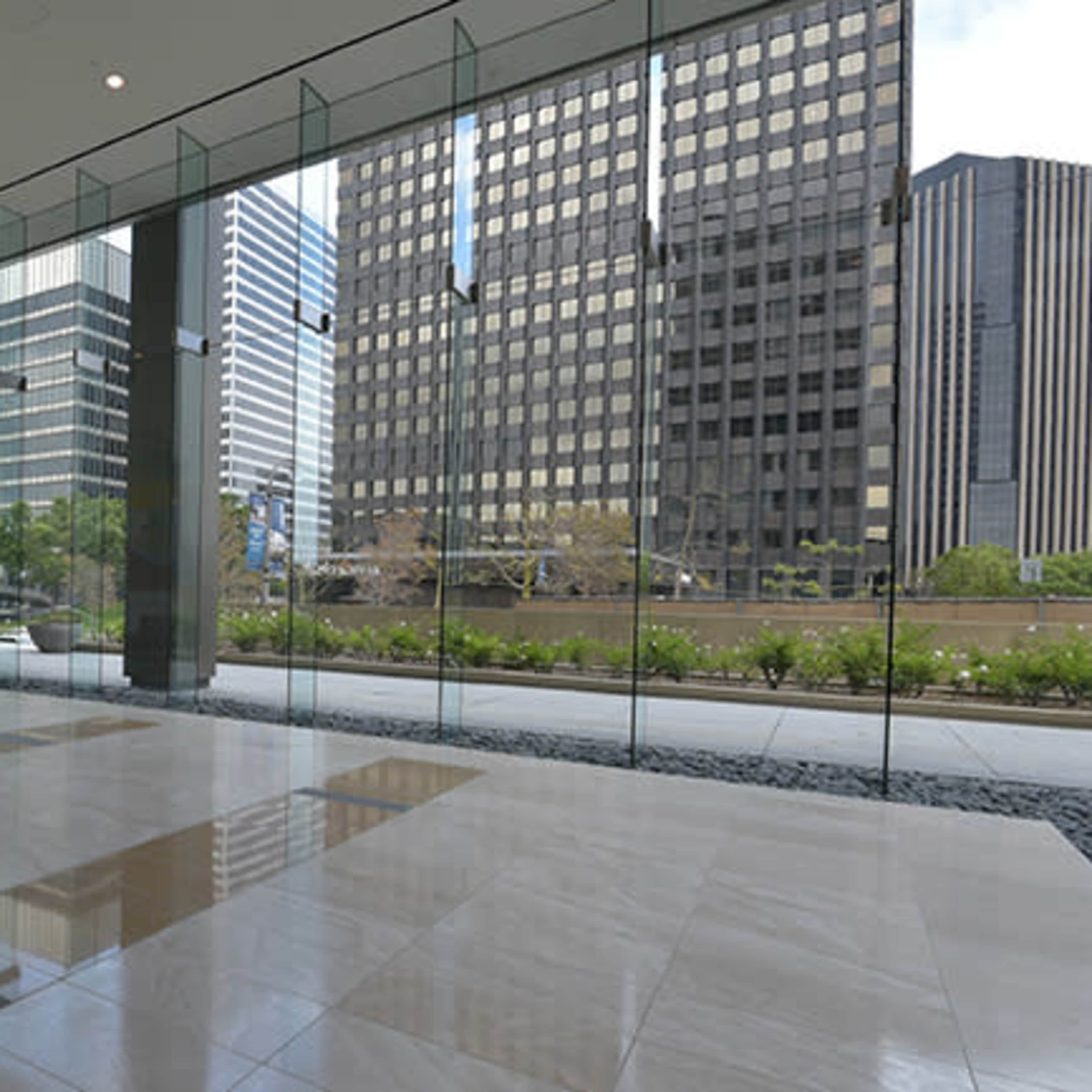 A modern interior lobby with large glass windows overlooking a city skyline and greenery.