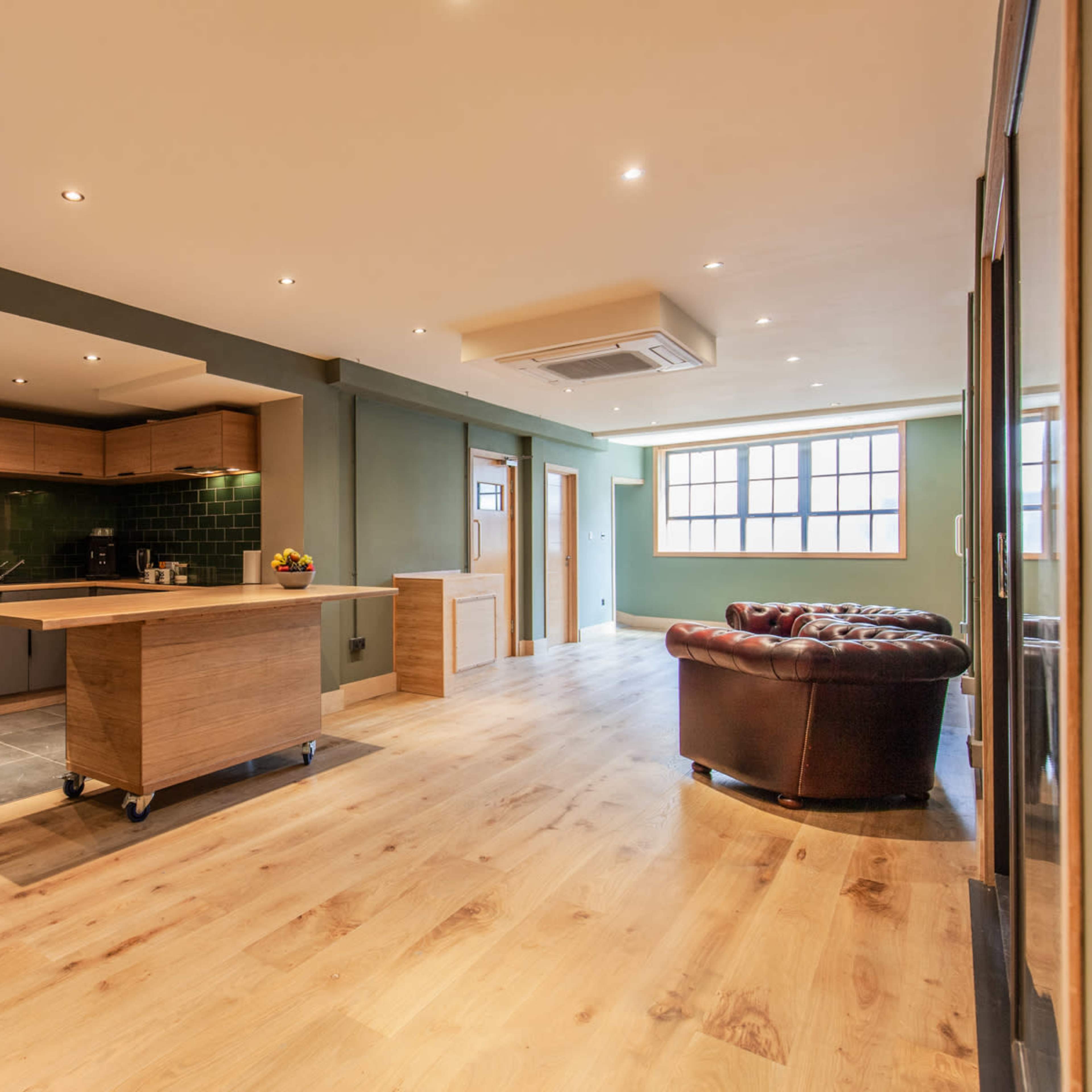 A spacious open-plan kitchen and living area with a wooden floor, modern cabinetry, and a leather seating arrangement.