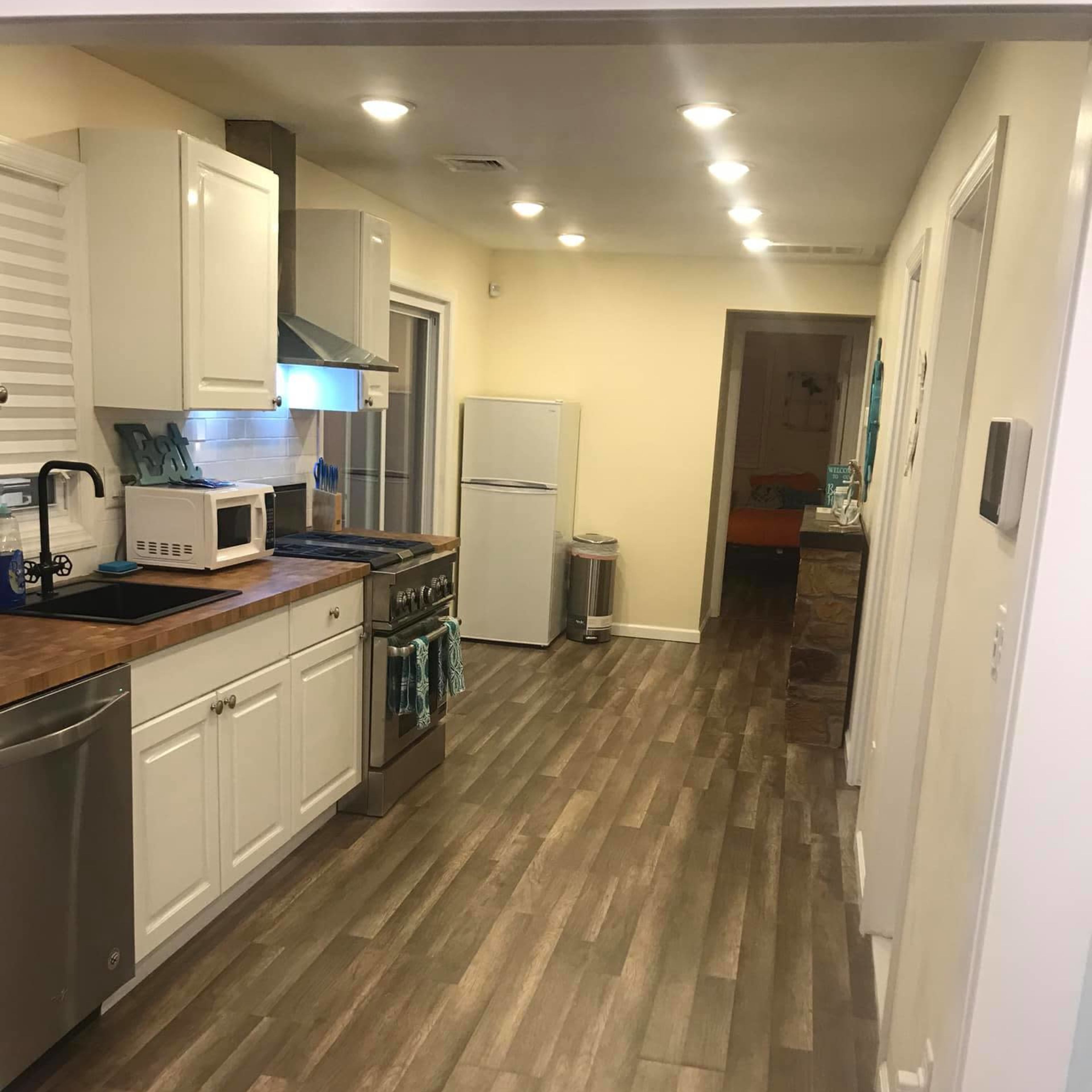 A modern kitchen with white cabinets, a stainless steel refrigerator, and a long corridor leading to a partially visible hallway.