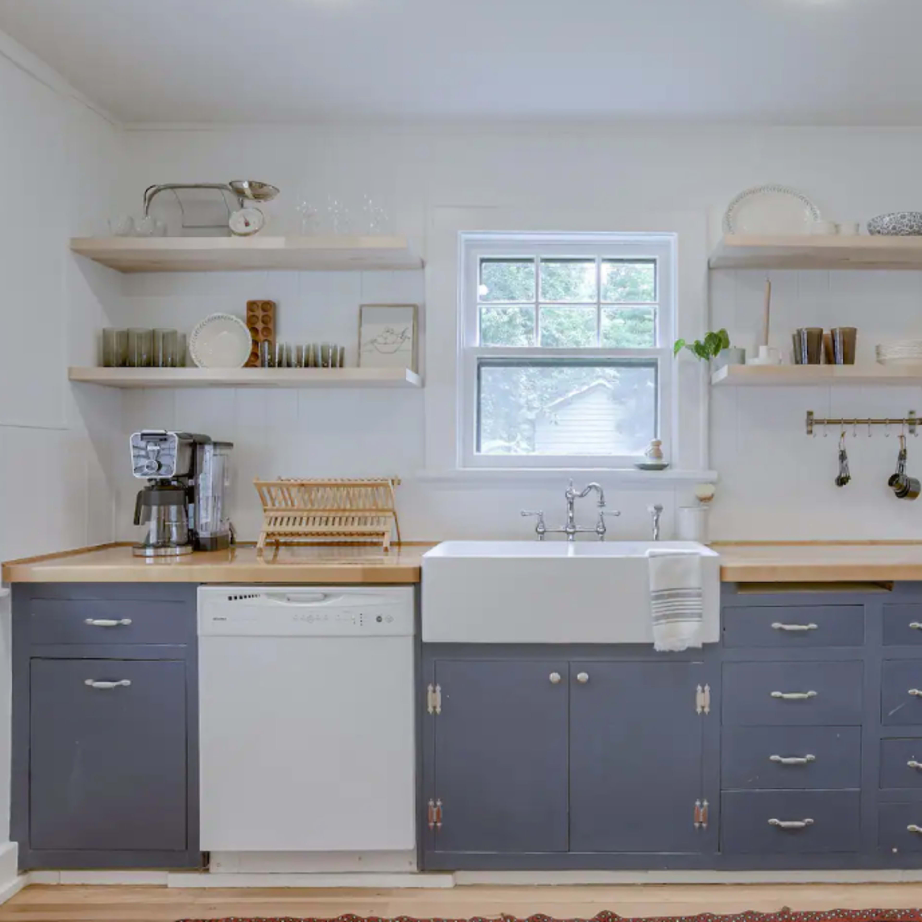 A modern kitchen with a farmhouse sink, open shelves displaying dishware, and blue cabinetry beneath a countertop.