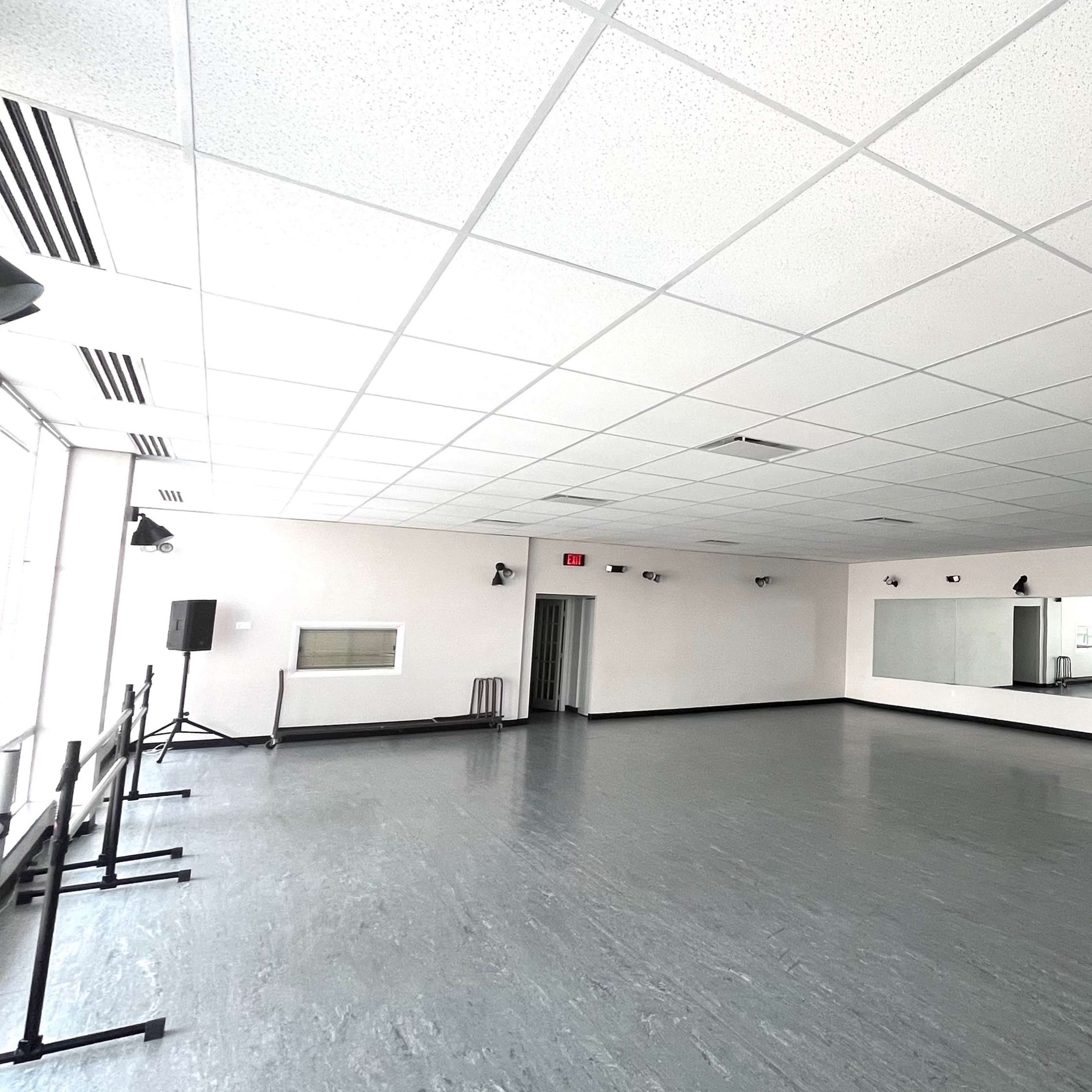A spacious dance studio features a smooth wooden floor, large mirrors, and wall-mounted lights.
