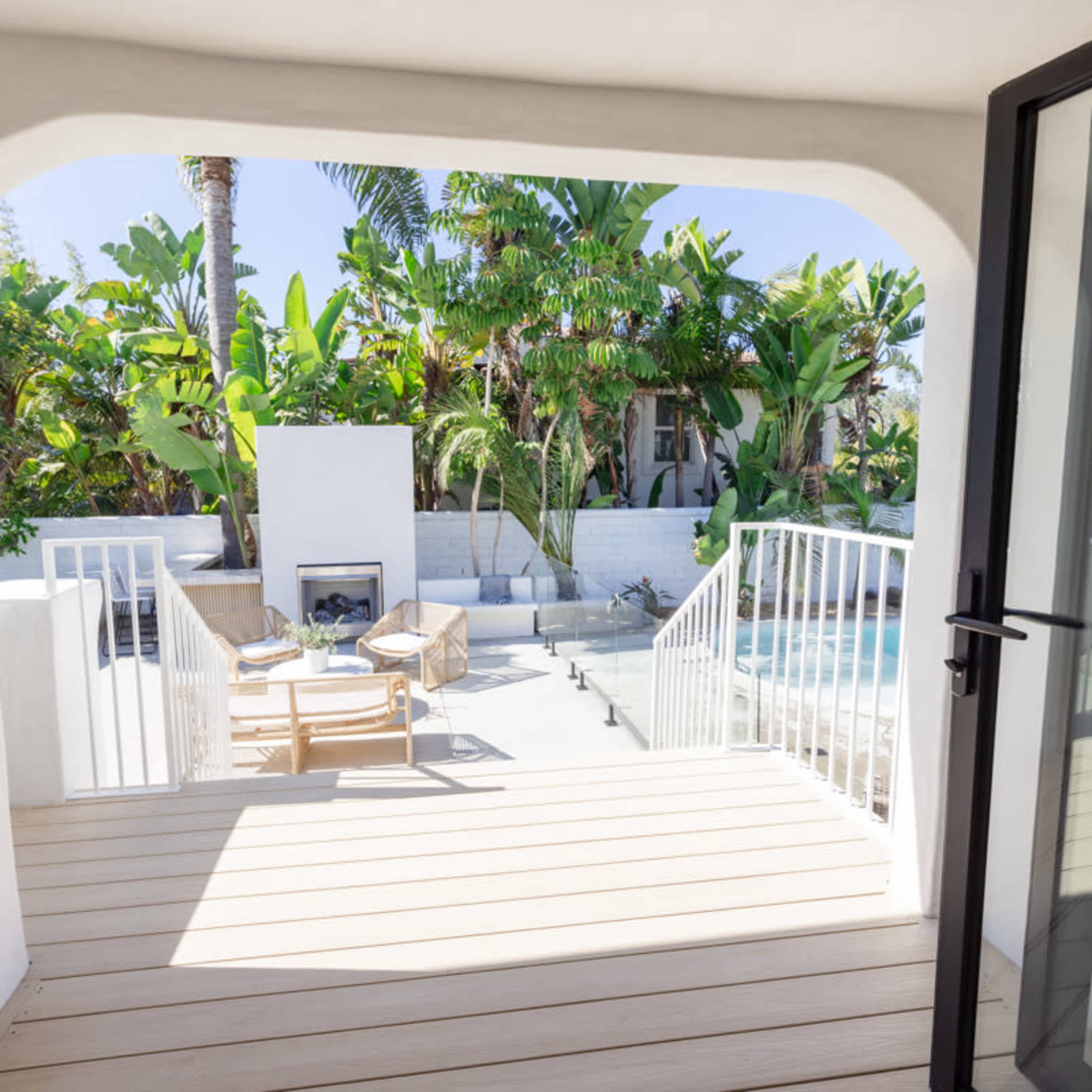 A spacious balcony with wooden decking overlooks a modern outdoor space featuring a pool, lounge chairs, and tropical plants.