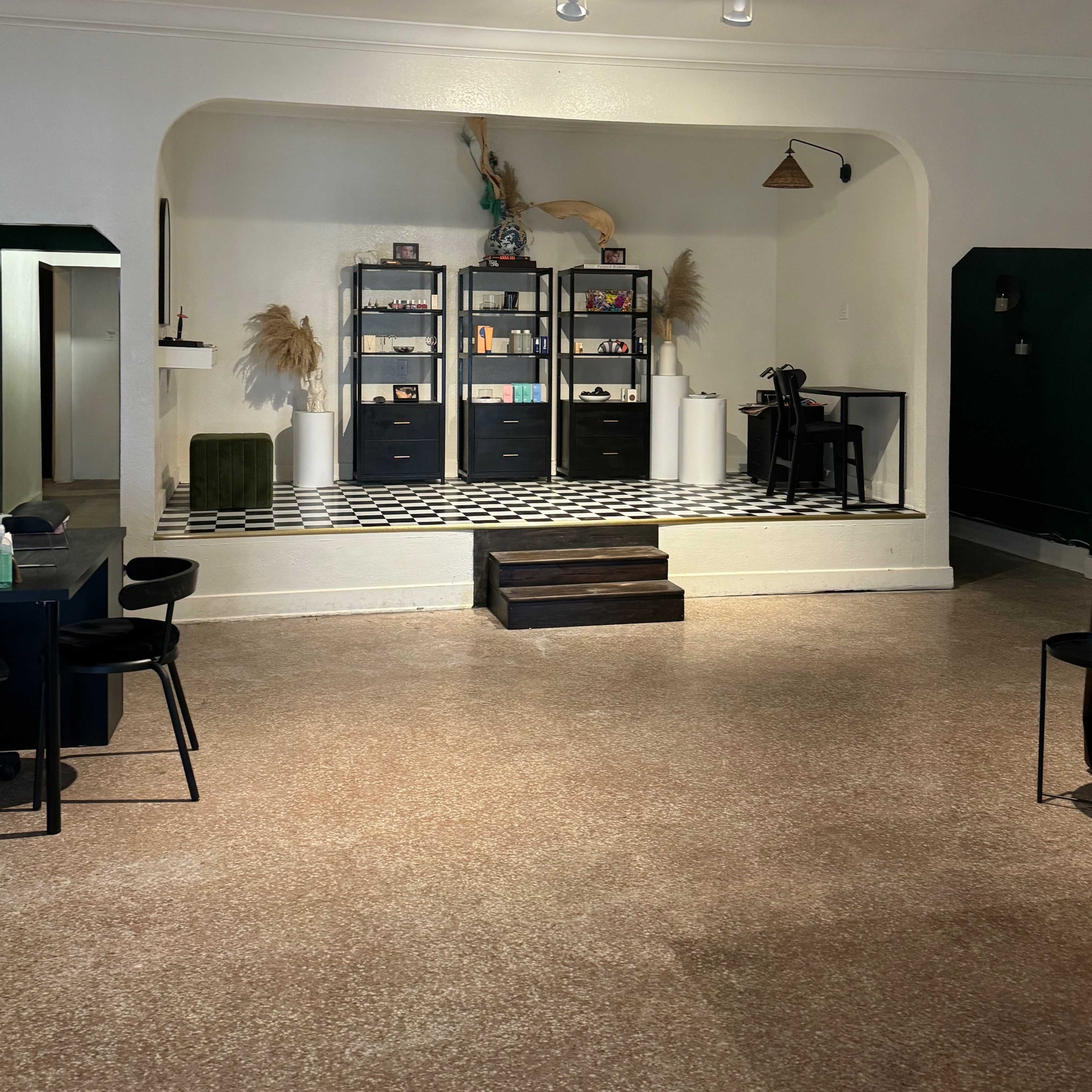 A stylish interior space featuring a raised platform with black shelves, decorative items, and patterned flooring, framed by a wall with dark green paint.