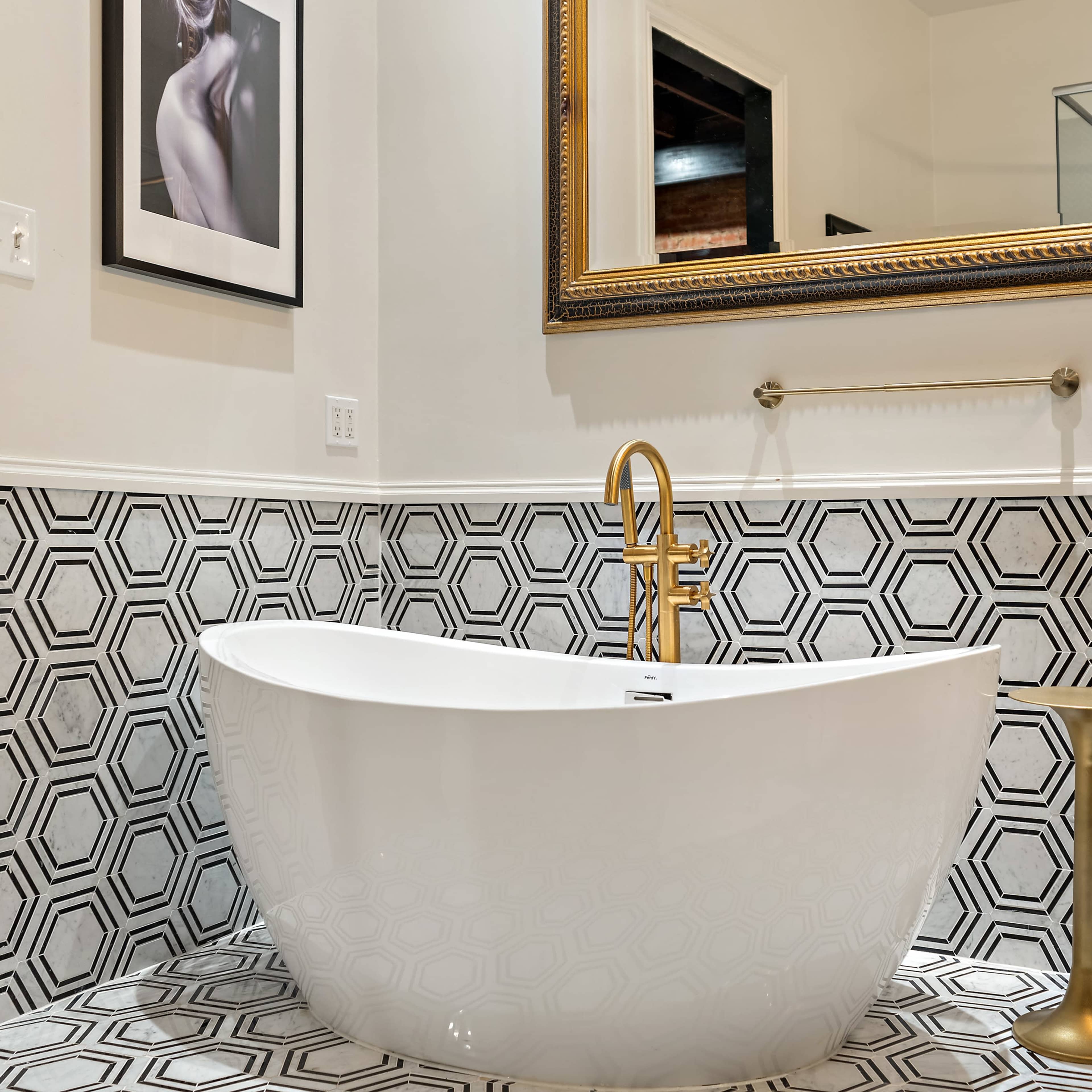 A modern bathroom featuring a freestanding white bathtub, hexagonal patterned tiles on the wall, and a large ornate mirror above the sink area.