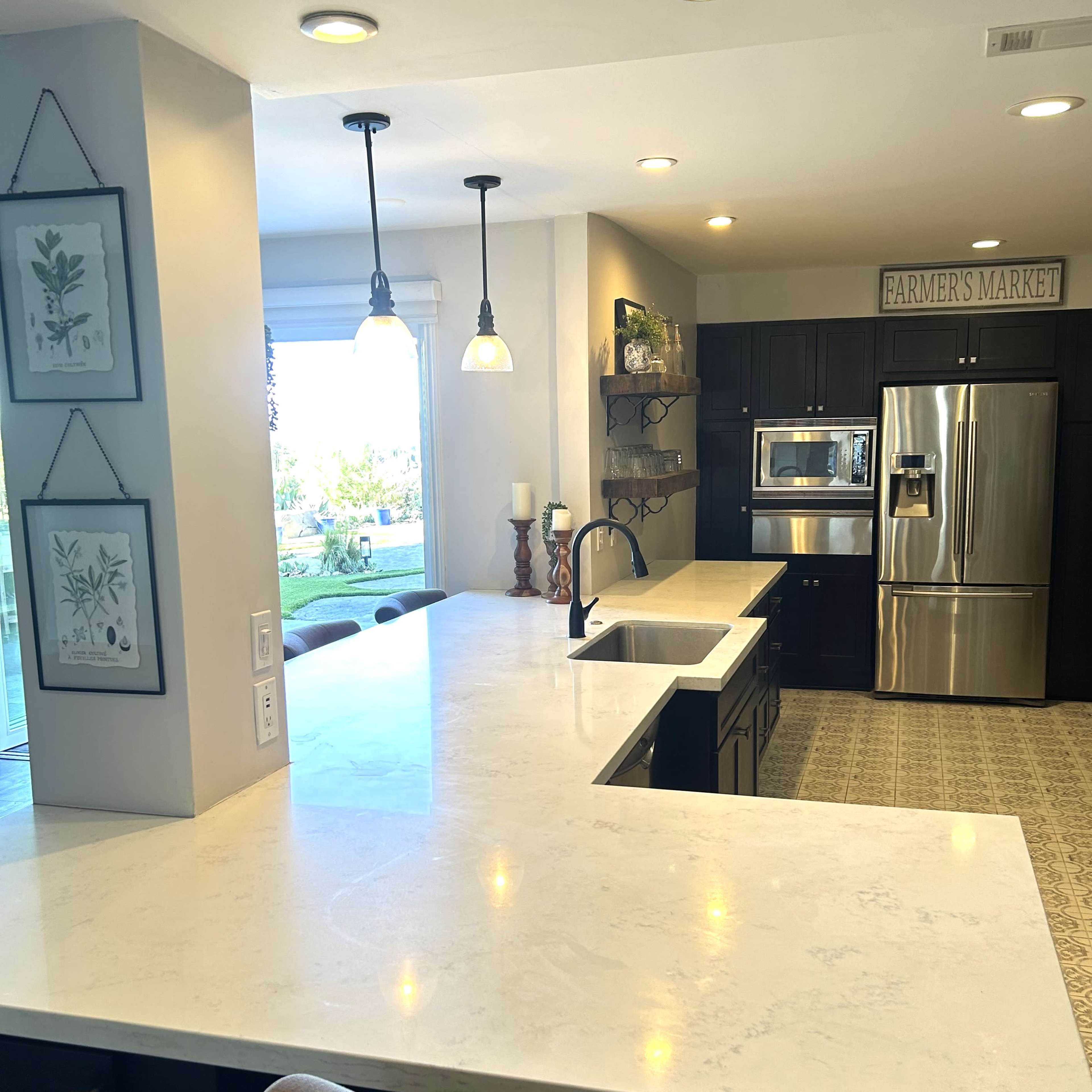 A modern kitchen with dark cabinetry, a light-colored countertop, and stainless steel appliances, featuring a window that allows natural light to enter the space.
