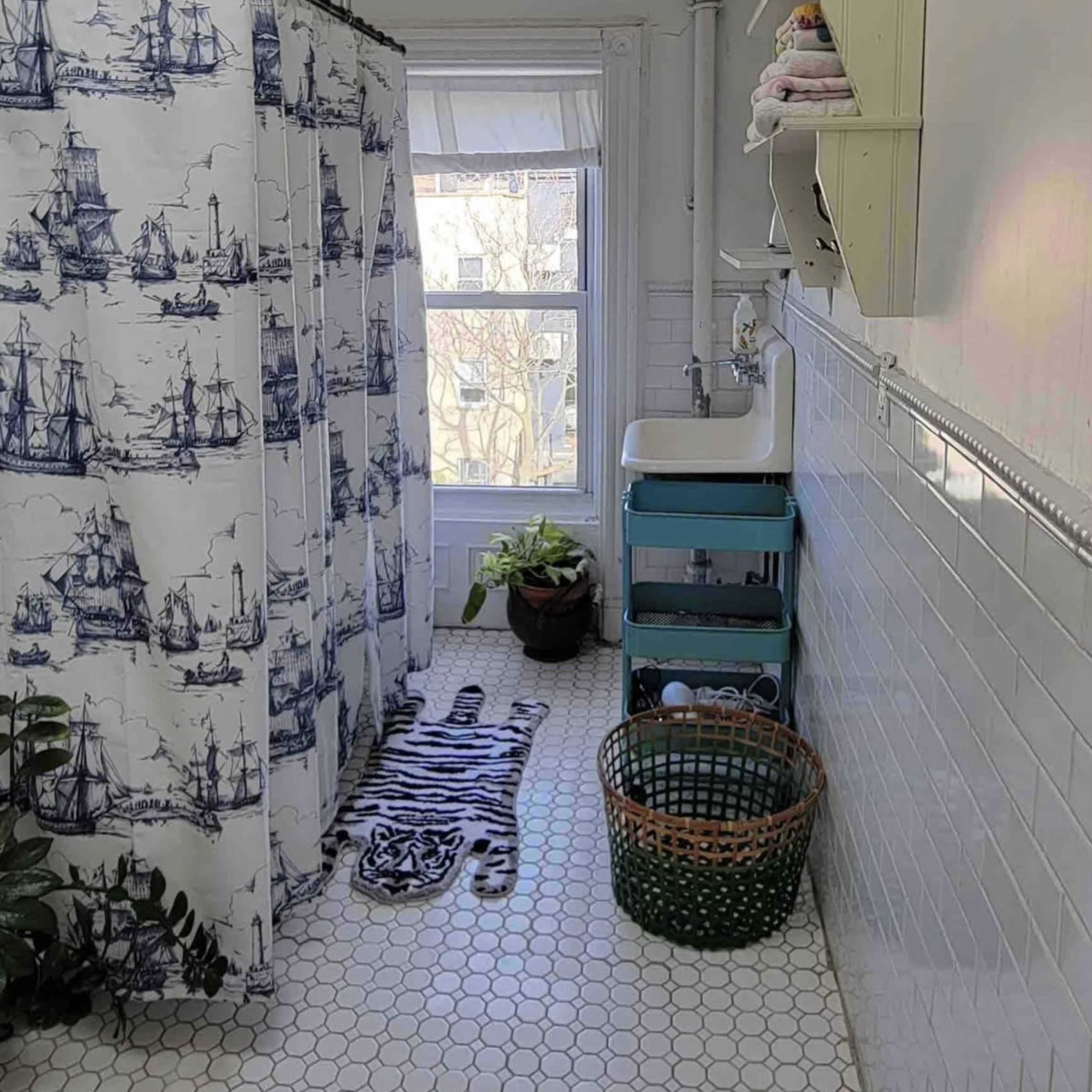 A bathroom features a patterned shower curtain, vintage sink, and potted plants near a window.