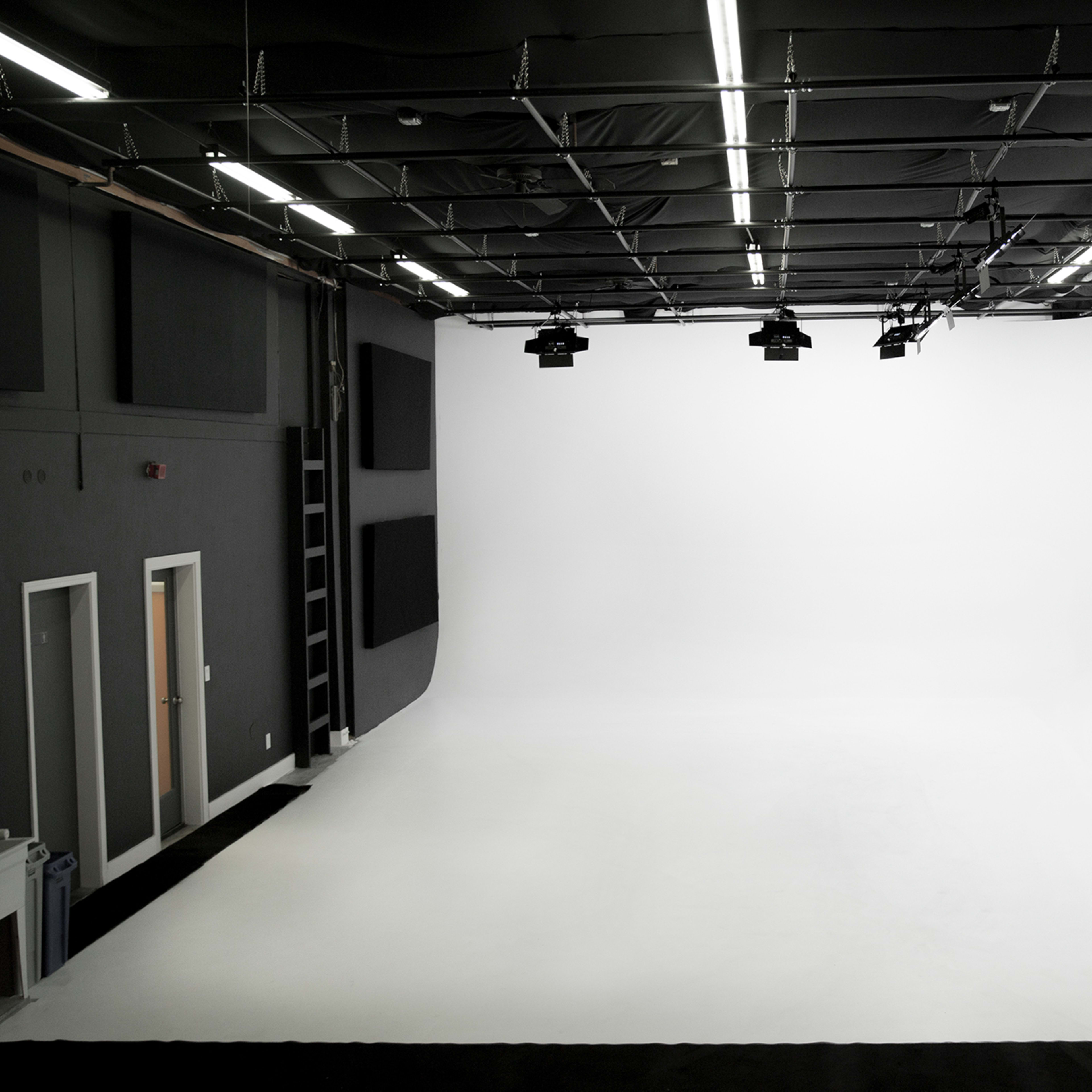 A spacious photography studio with a seamless white backdrop and overhead lighting.