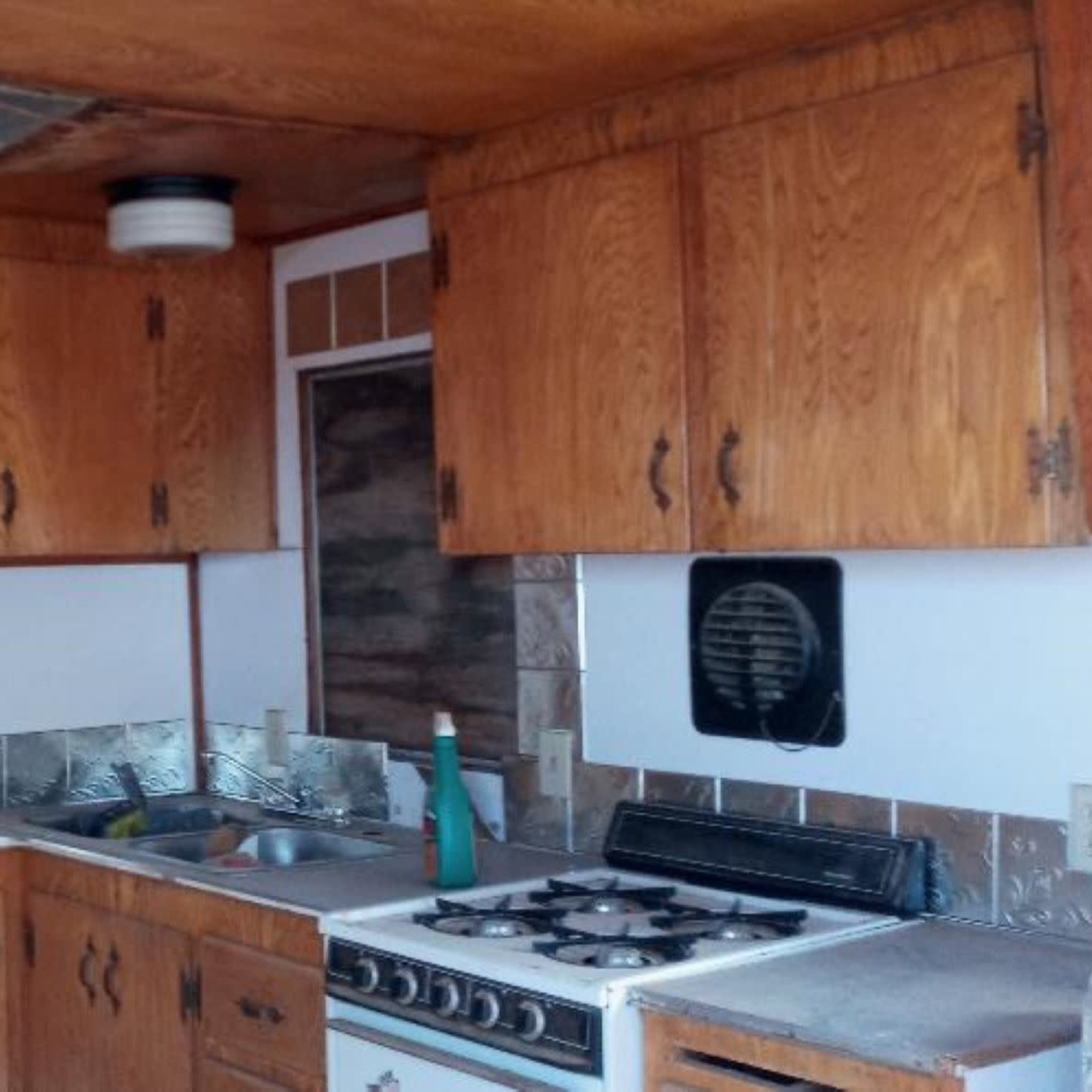 A wooden kitchen with brown cabinetry, a gas stove, and a small sink area.