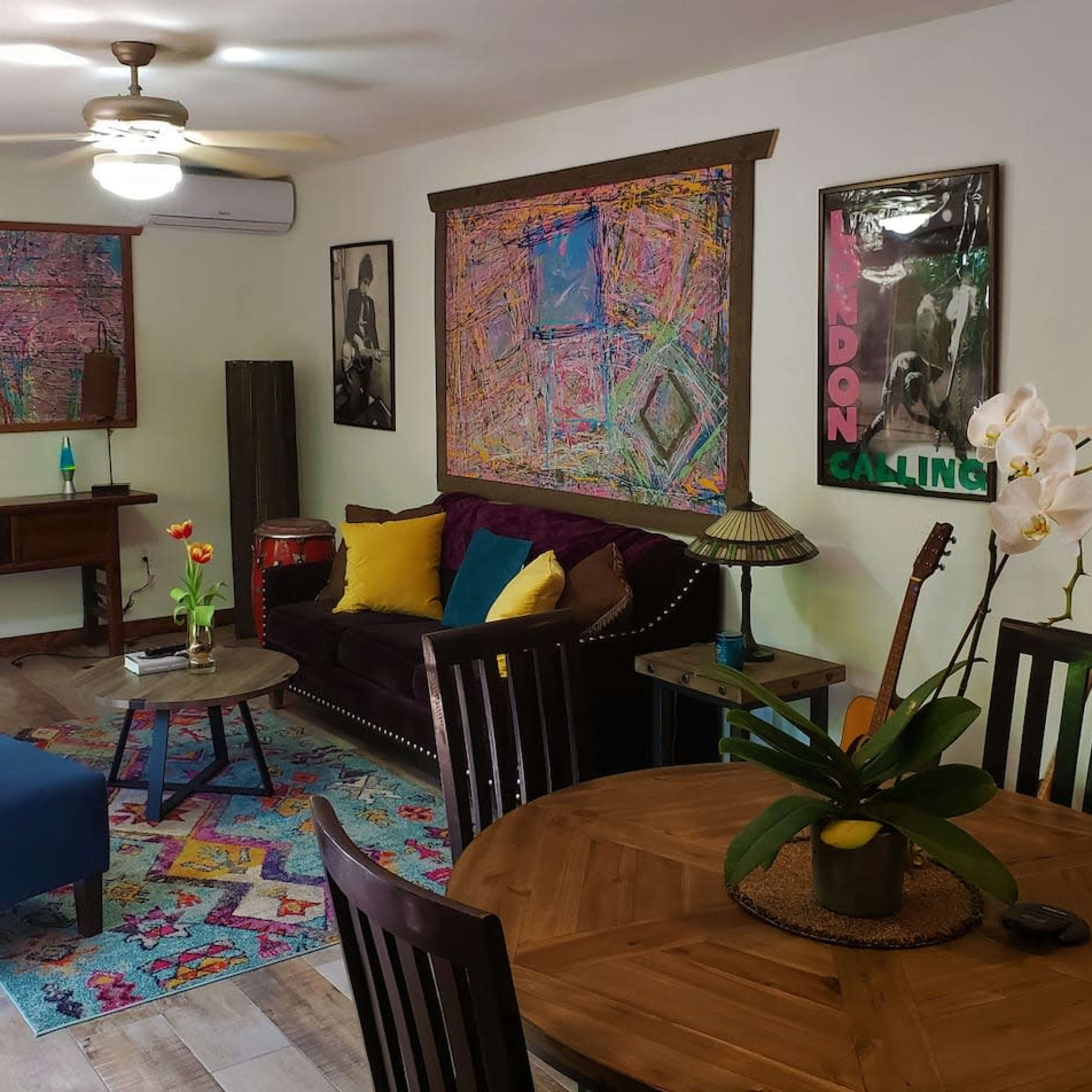 The room features a seating area with a purple couch, blue chairs, a wooden table, and colorful abstract artwork on the walls.