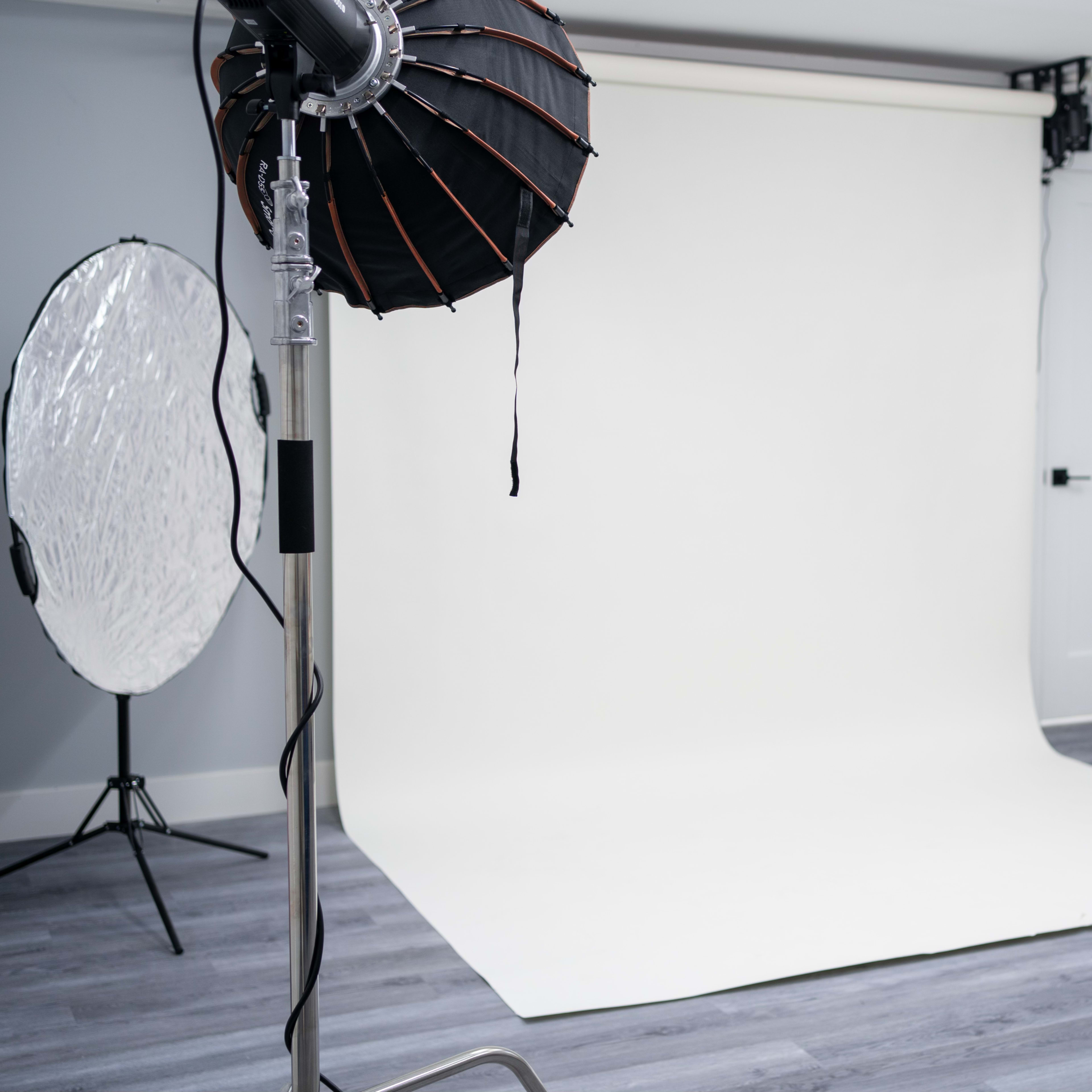 A photography studio with a white backdrop, lighting equipment, and a round reflector.