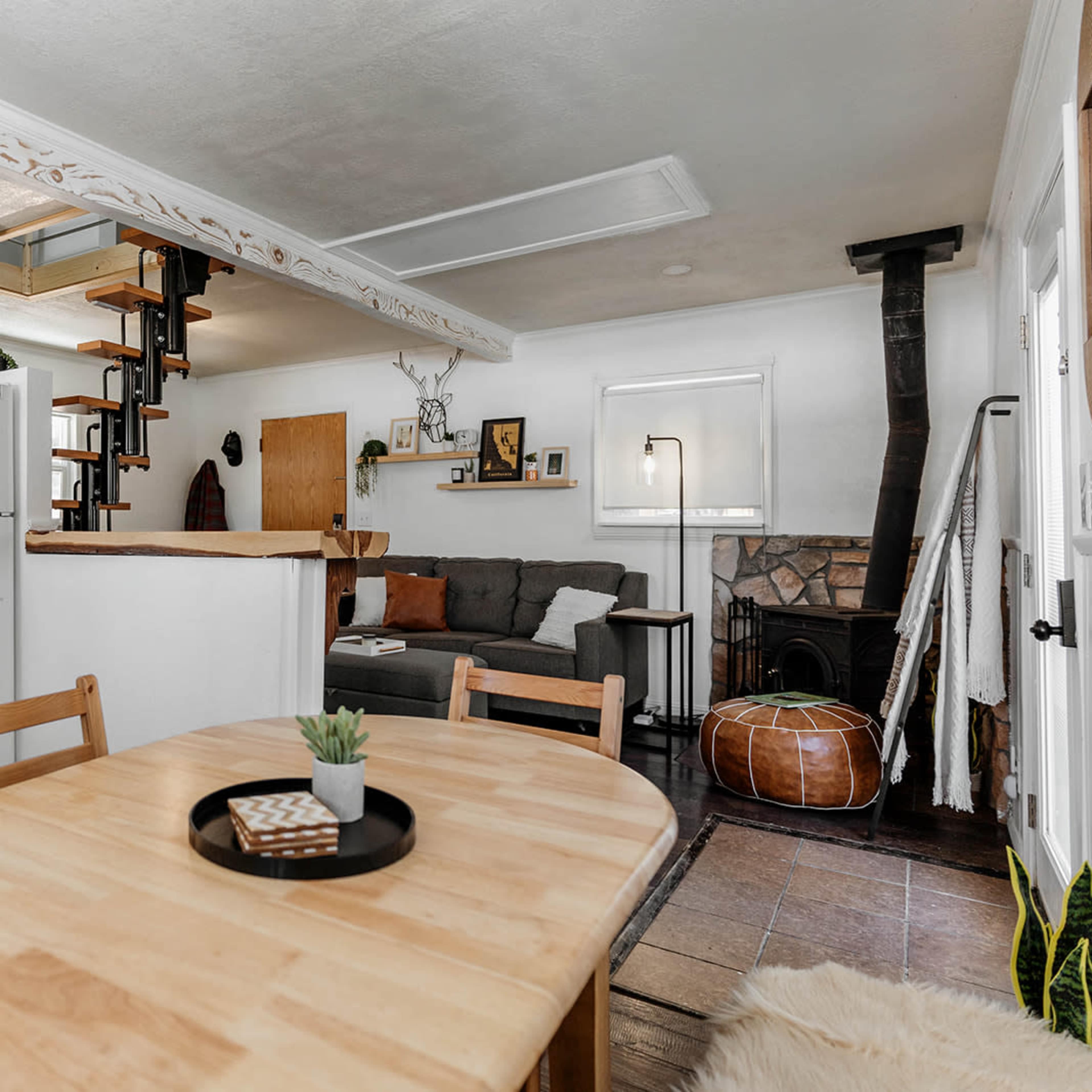 A cozy interior space featuring a kitchen with white cabinets, a dining table, a living area with a gray sofa, and a staircase leading to an upper level.