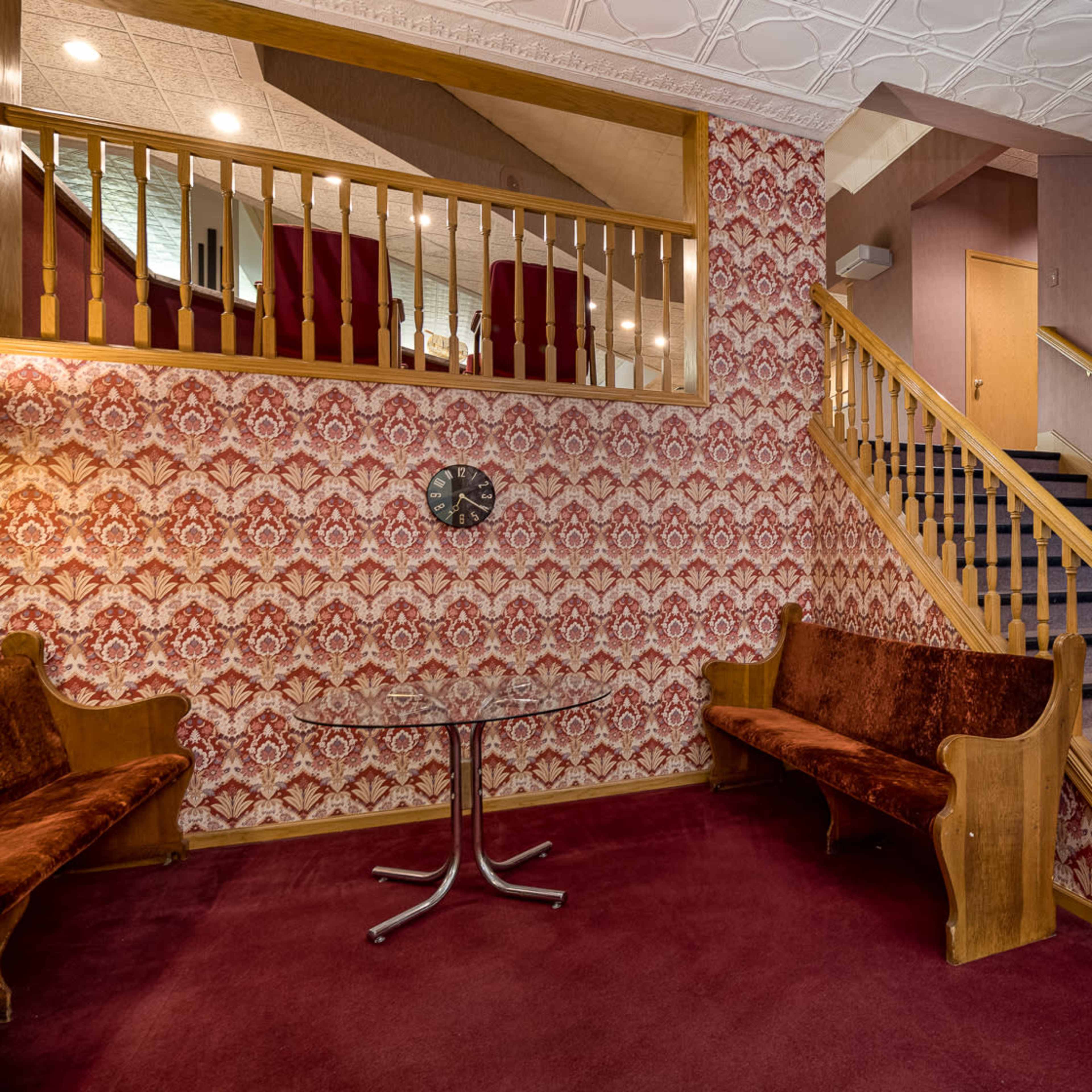 A foyer with patterned wallpaper, two brown upholstered benches, a round table, and a staircase leading to an upper level.
