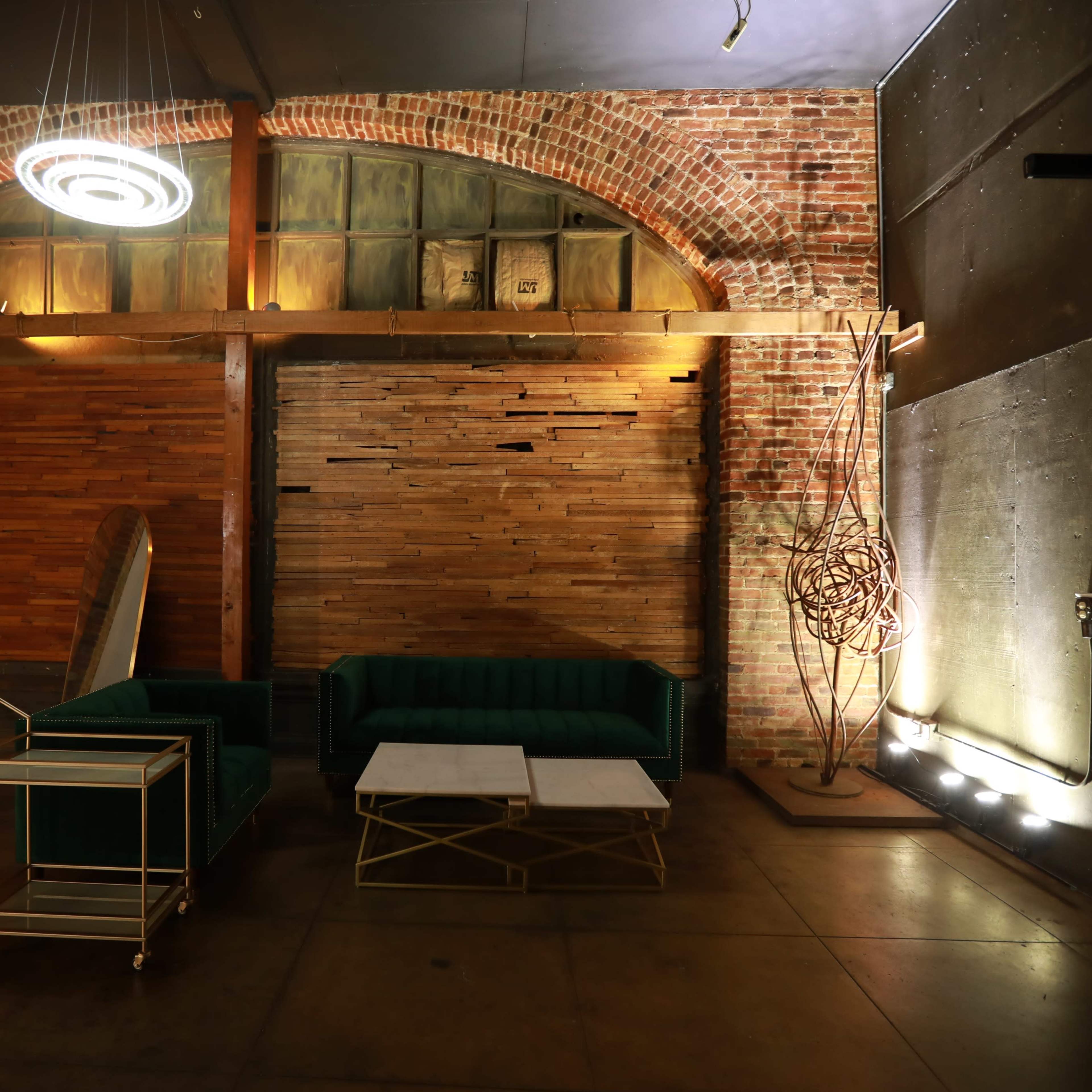 A modern interior space with a brick wall, wooden paneling, a green couch, two coffee tables, and ambient lighting.