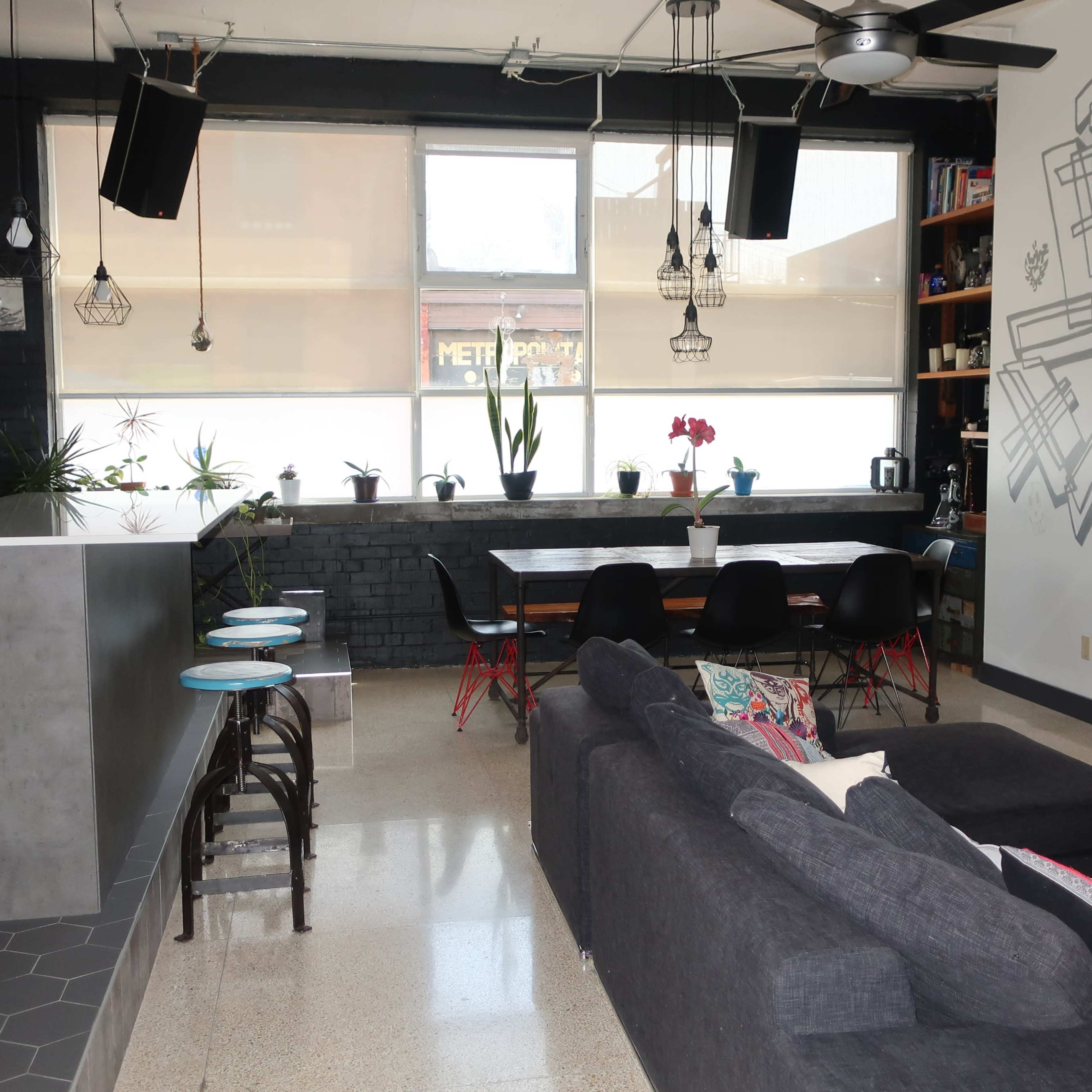 A modern open-concept living space with a kitchen area on the left and a dining area with a large table and chairs on the right, accented by a wall mural.