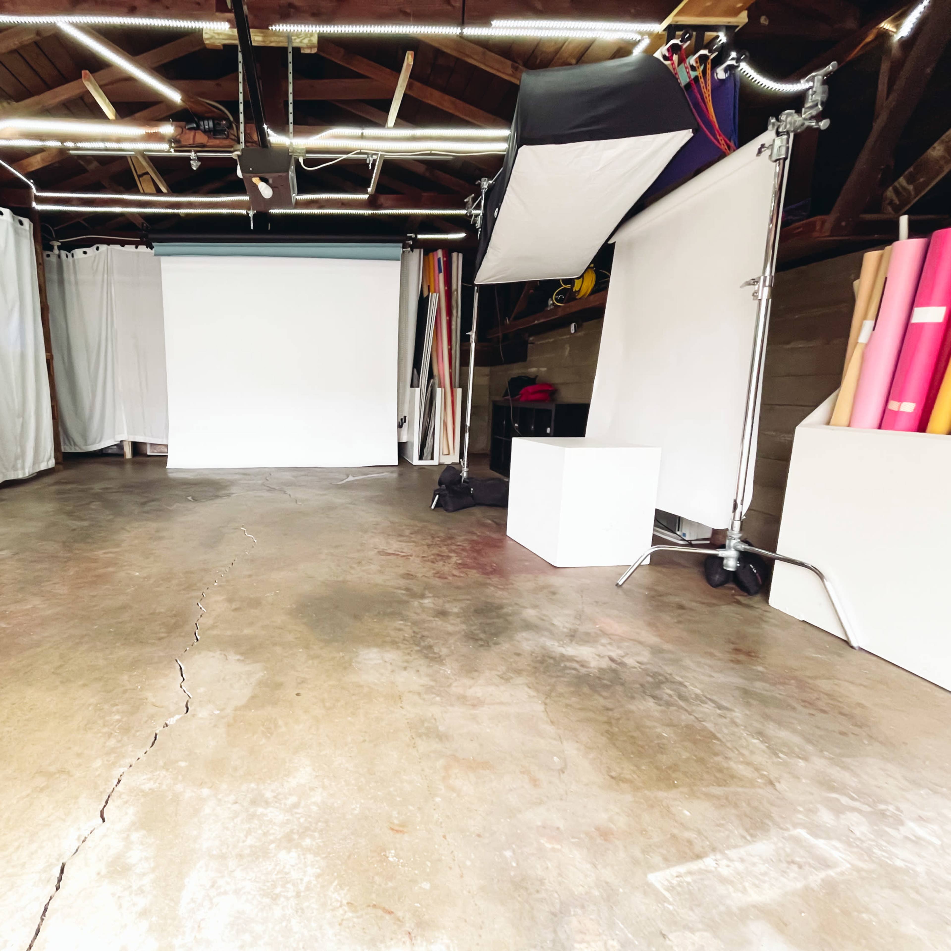 A spacious garage with a concrete floor, white curtains, and photography equipment arranged on either side.