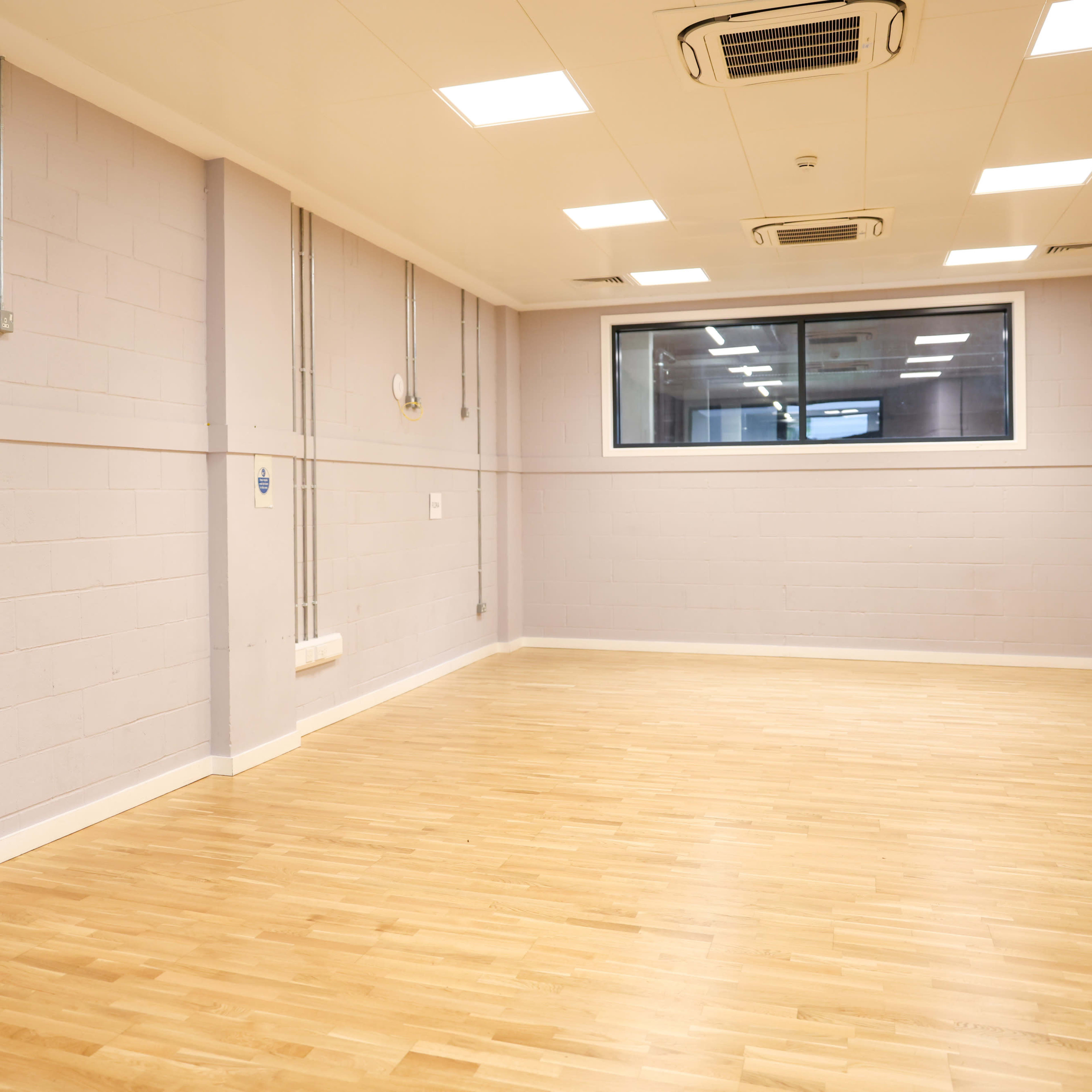 A spacious, empty room with light wood flooring and a door labeled "Kitchen" on one wall.