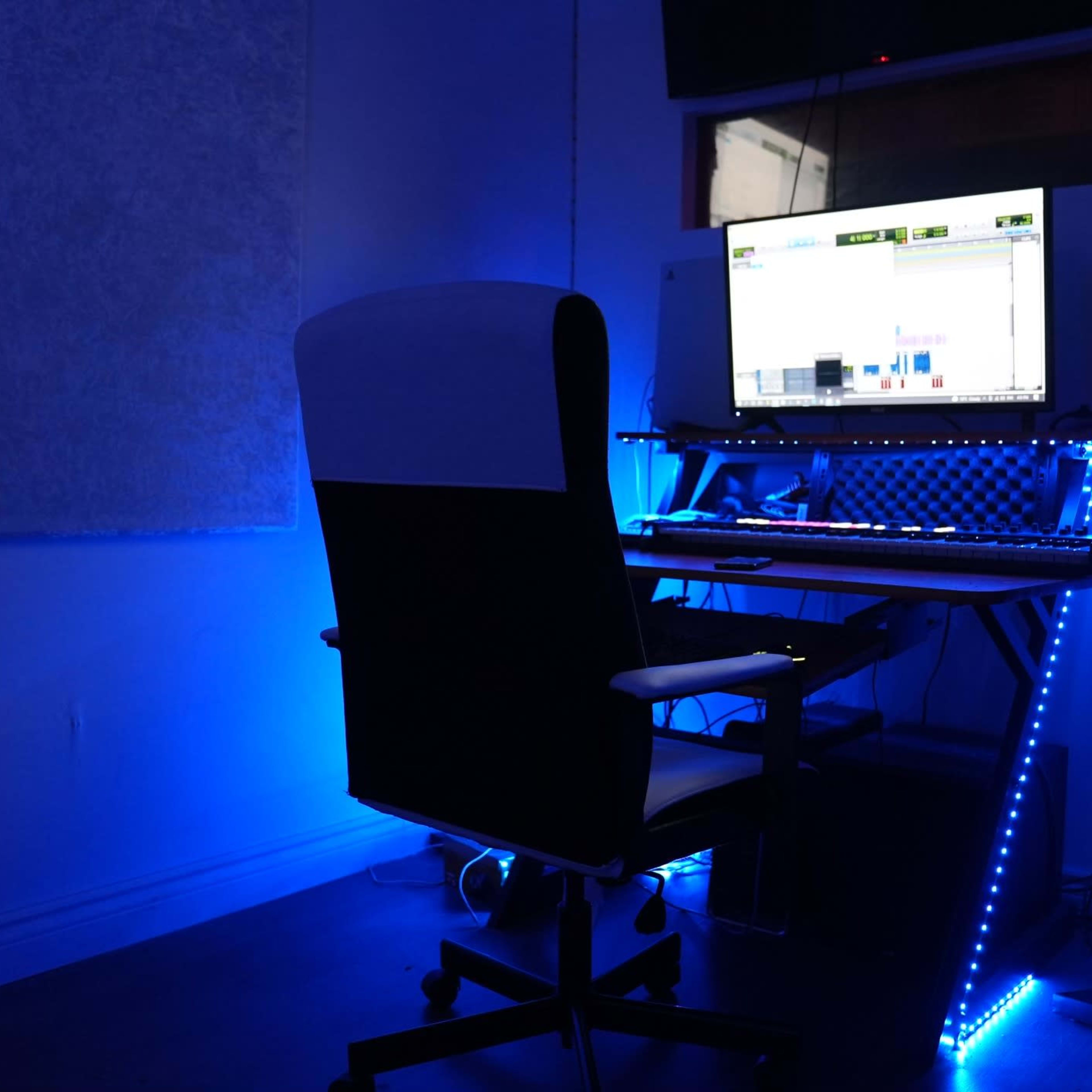 A music production workspace features a computer monitor, keyboard, and speakers illuminated by blue LED lights.
