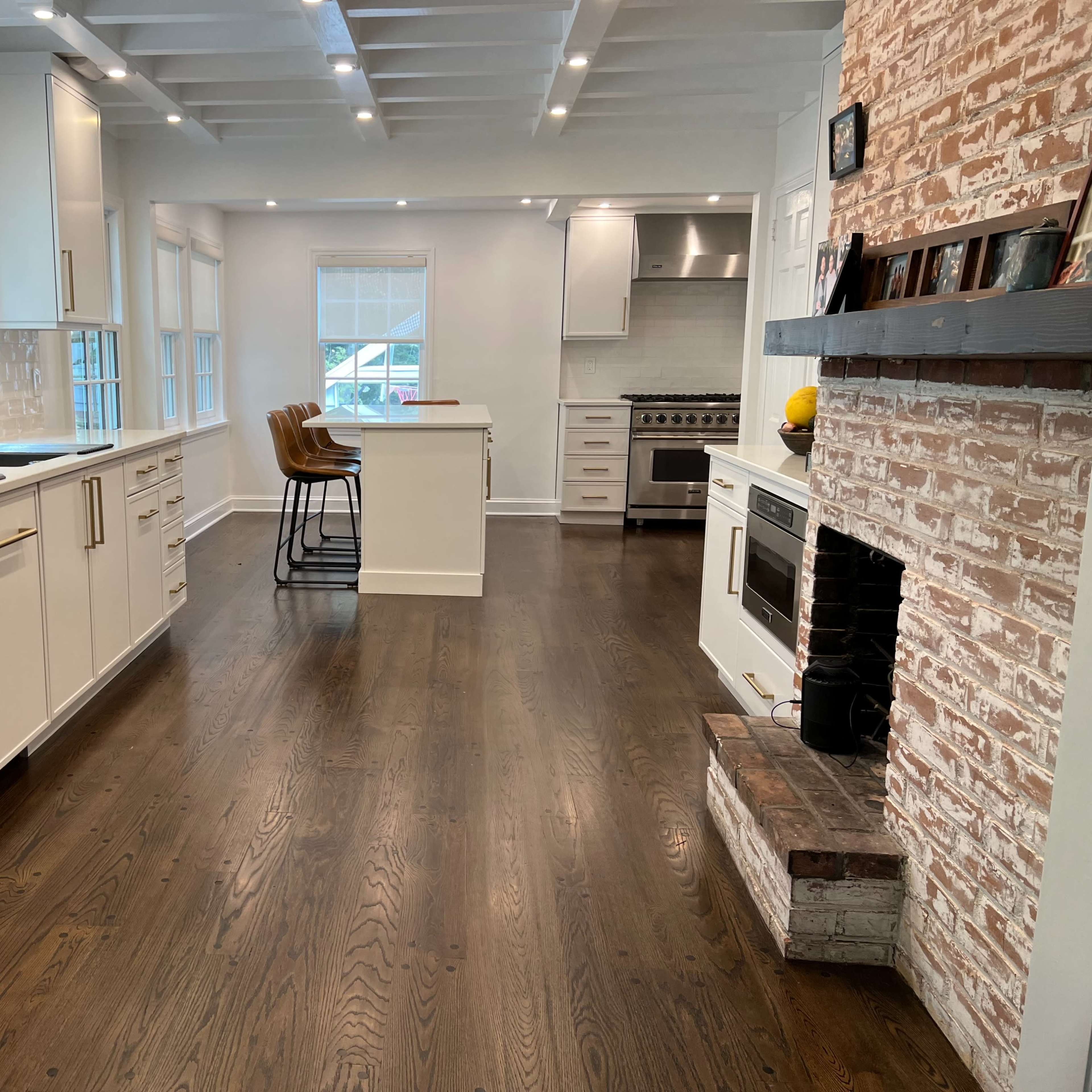 A modern kitchen features white cabinetry, a central island with bar stools, and wide hardwood flooring.