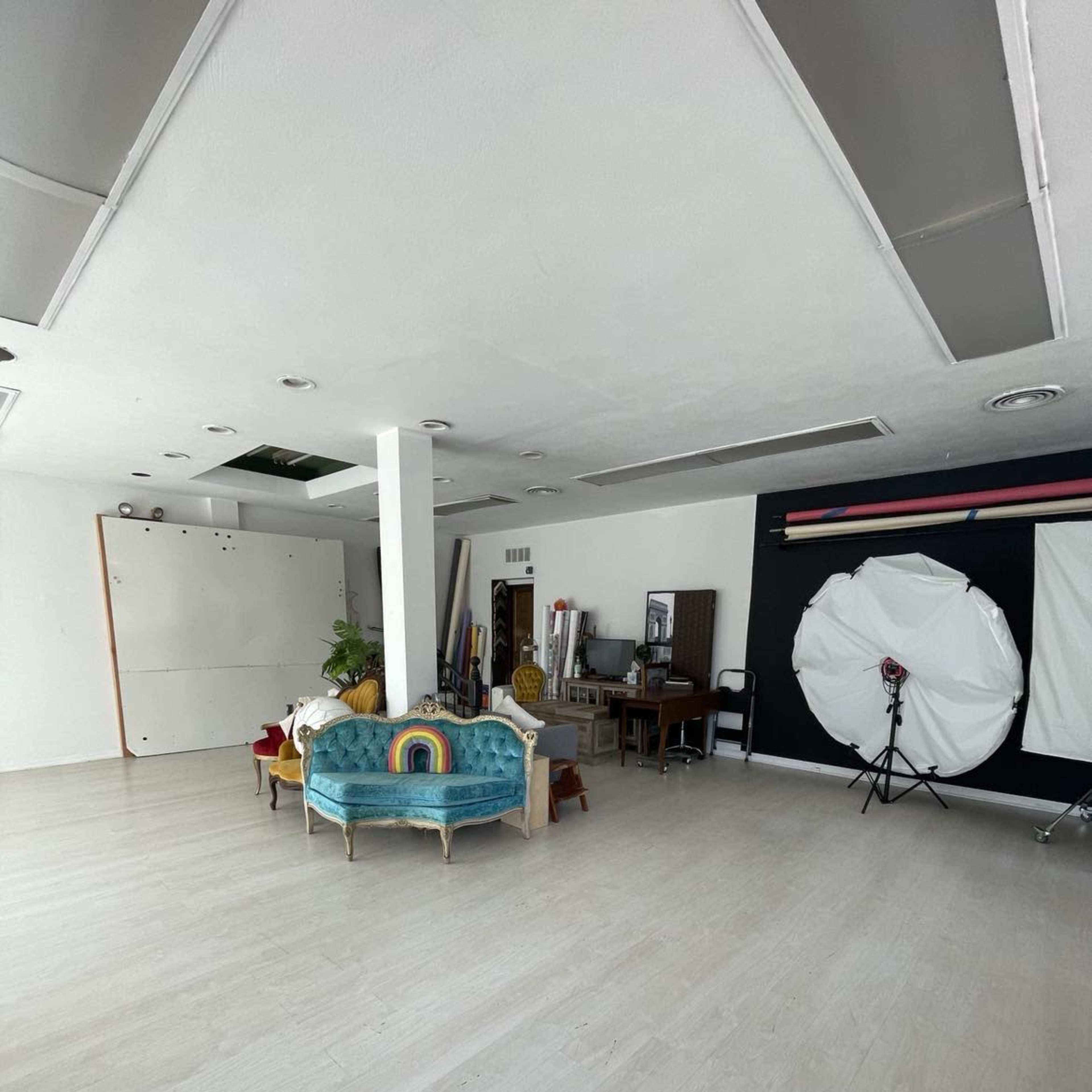 A spacious, empty room featuring a vintage sofa with a rainbow design, along with various photography equipment and a large backdrop setup.