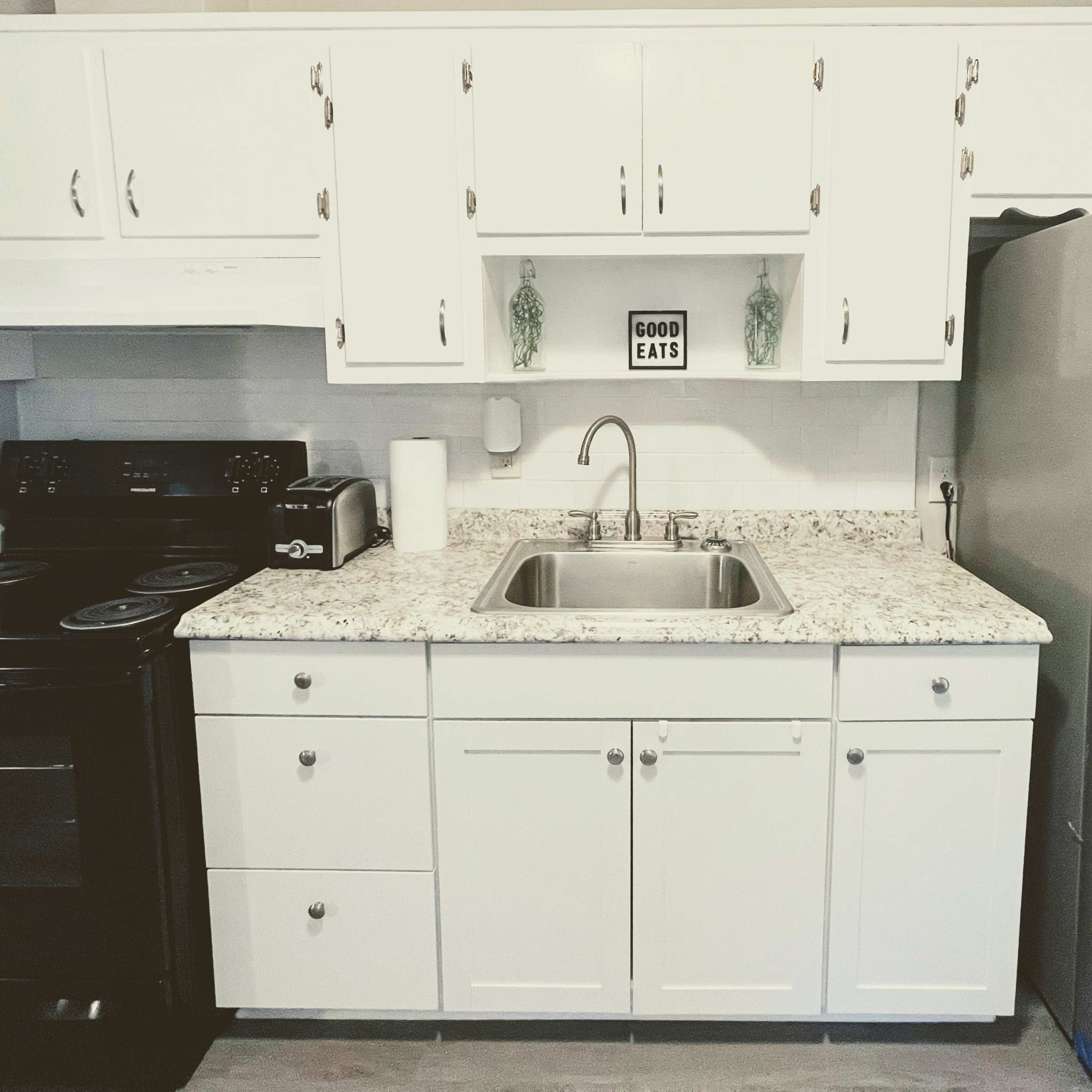 A kitchen with white cabinets, a black stove, a stainless steel refrigerator, and a granite countertop with a sink.