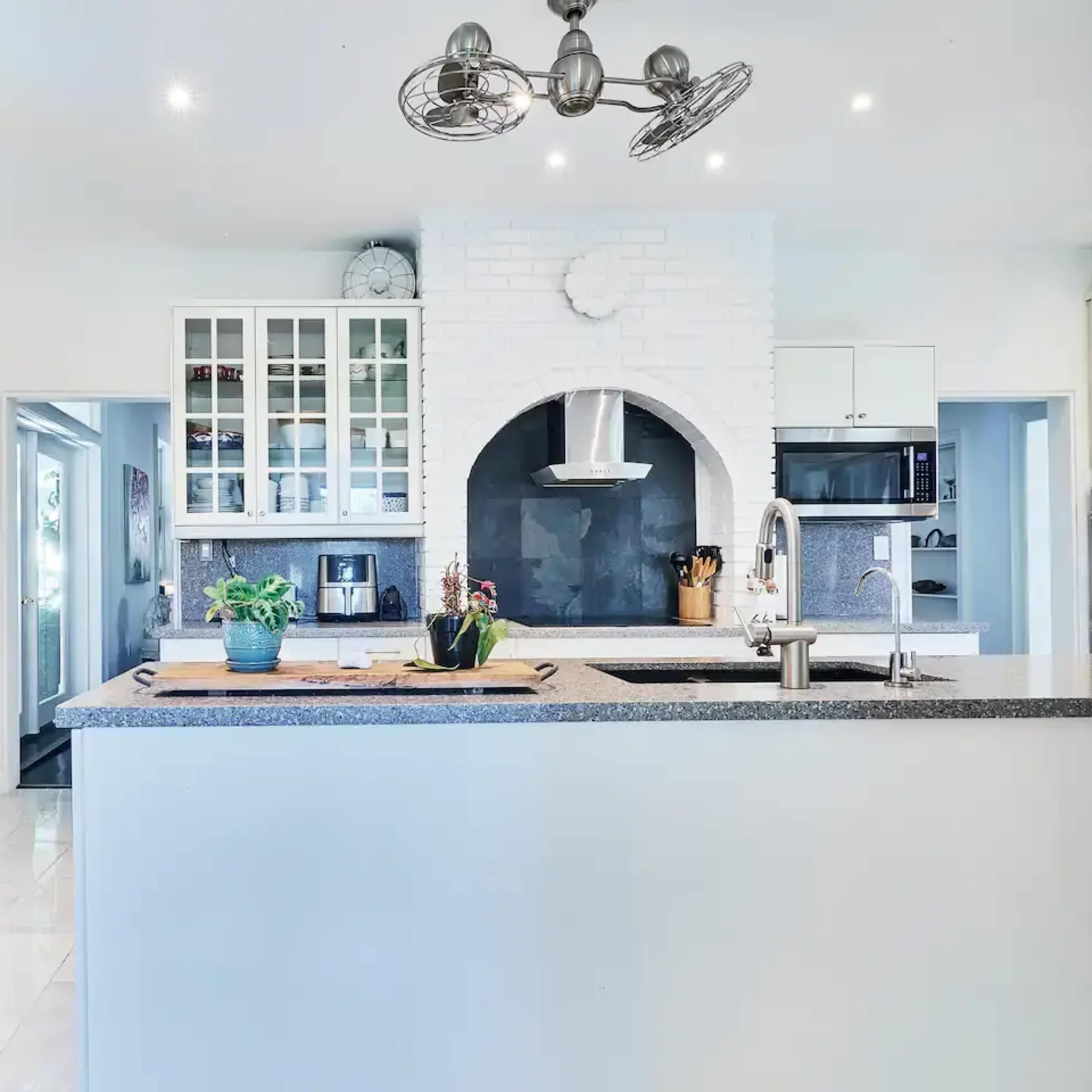 A modern kitchen with a central island, white cabinetry, and a slate grey countertop featuring a built-in stovetop and hood.