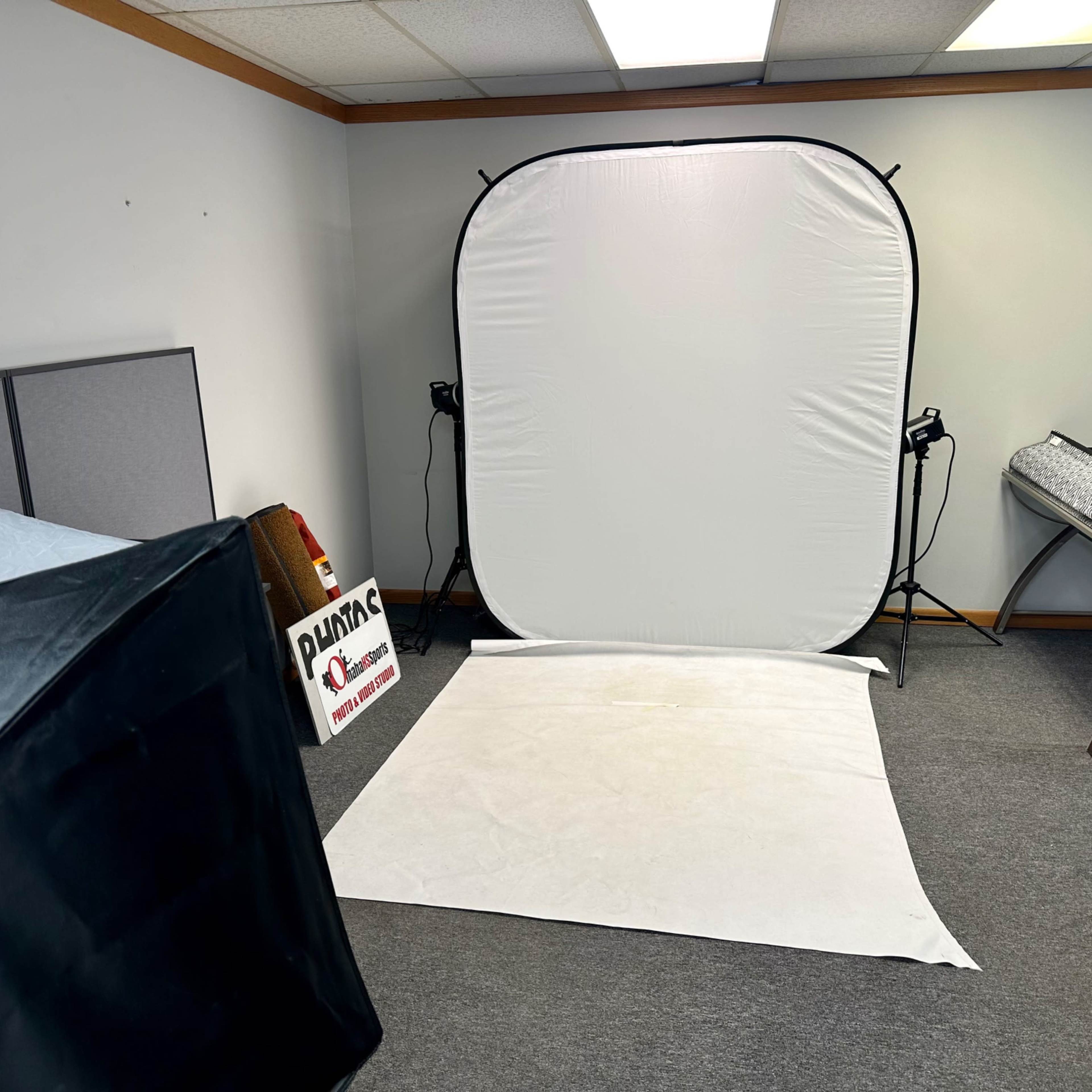 A room with a plain white backdrop setup for photography, along with a black tent and various equipment.