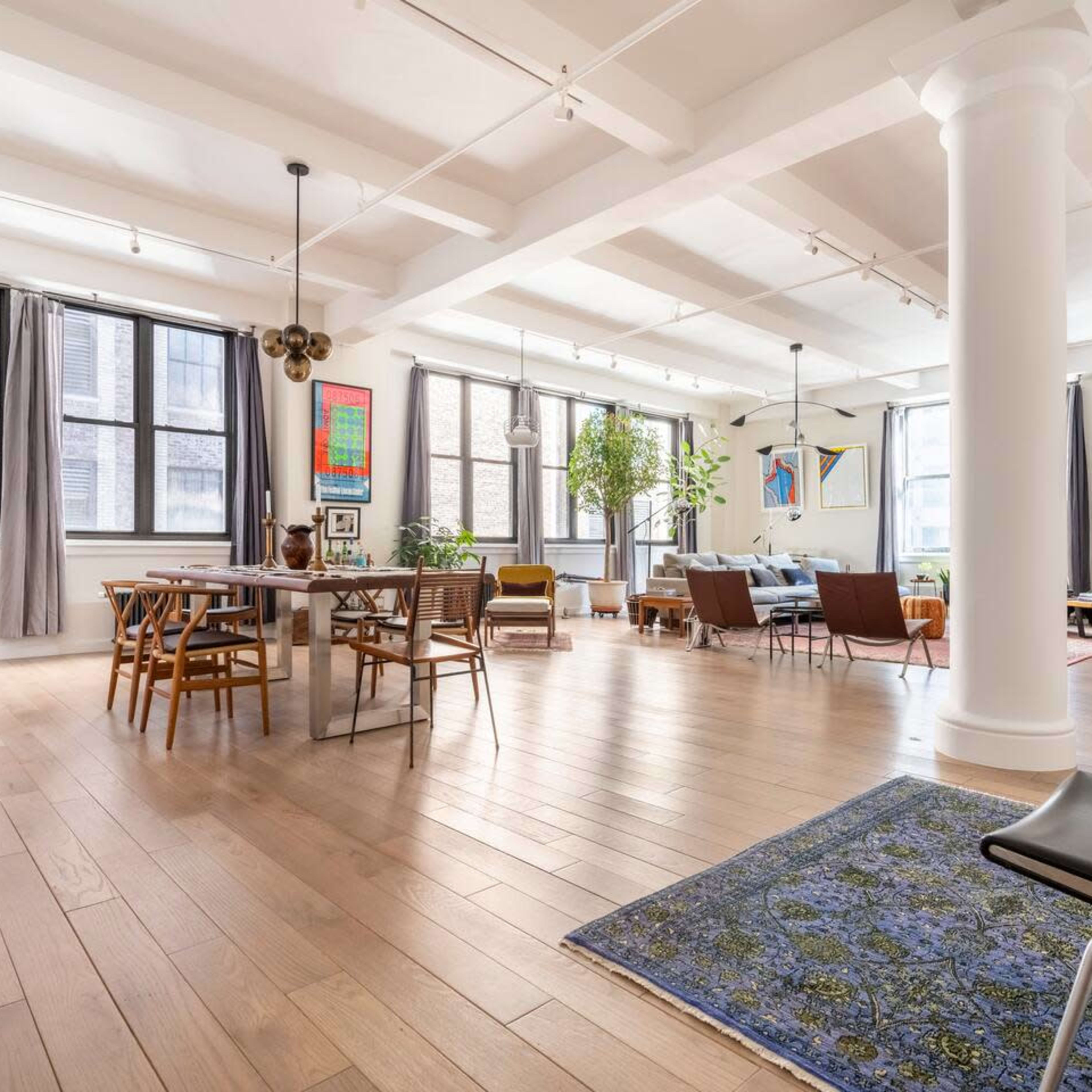 A spacious open-plan living area with hardwood floors, large windows, and a mix of dining and lounge furniture.
