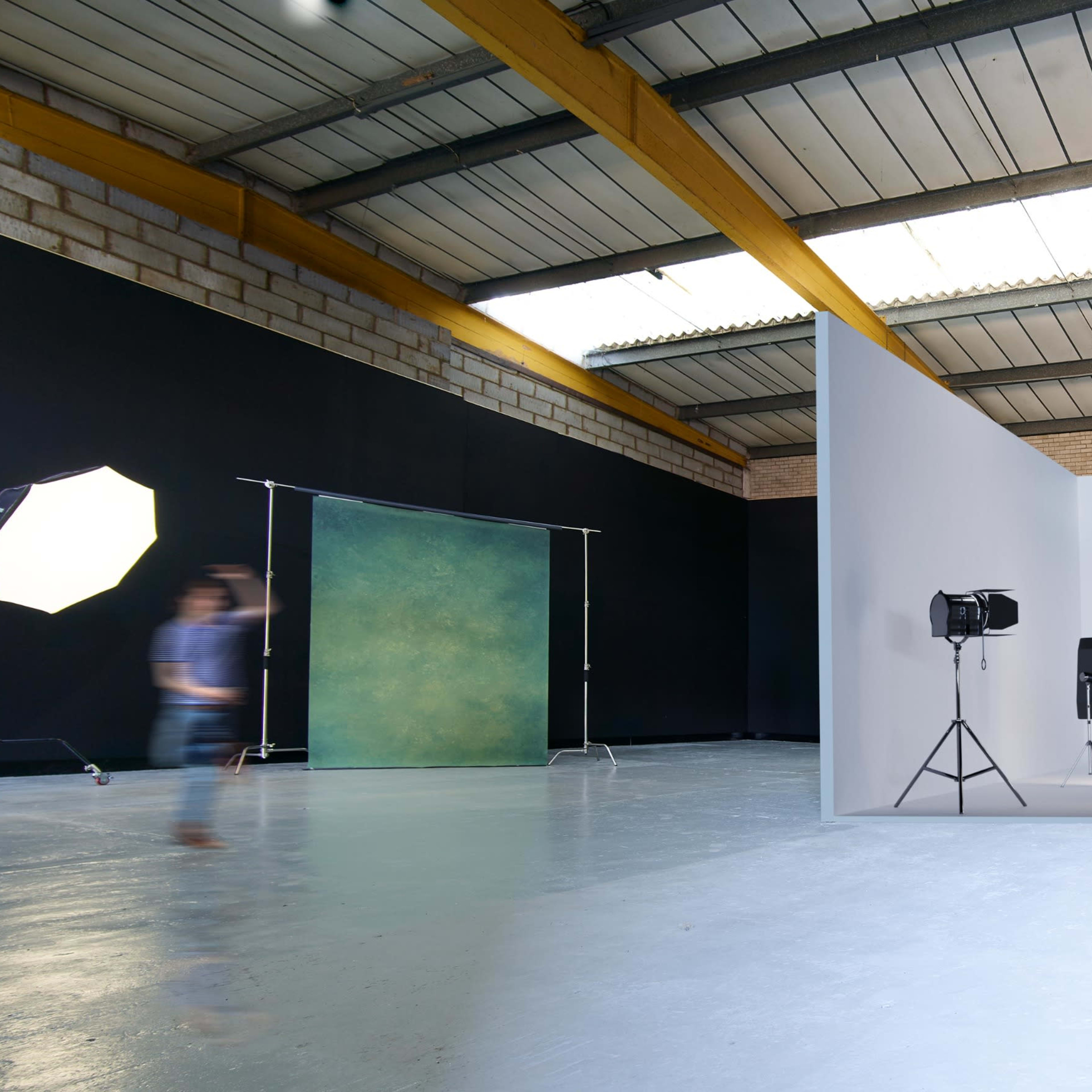 A spacious photography studio with a white background setup, lighting equipment, and a dark backdrop in the background.