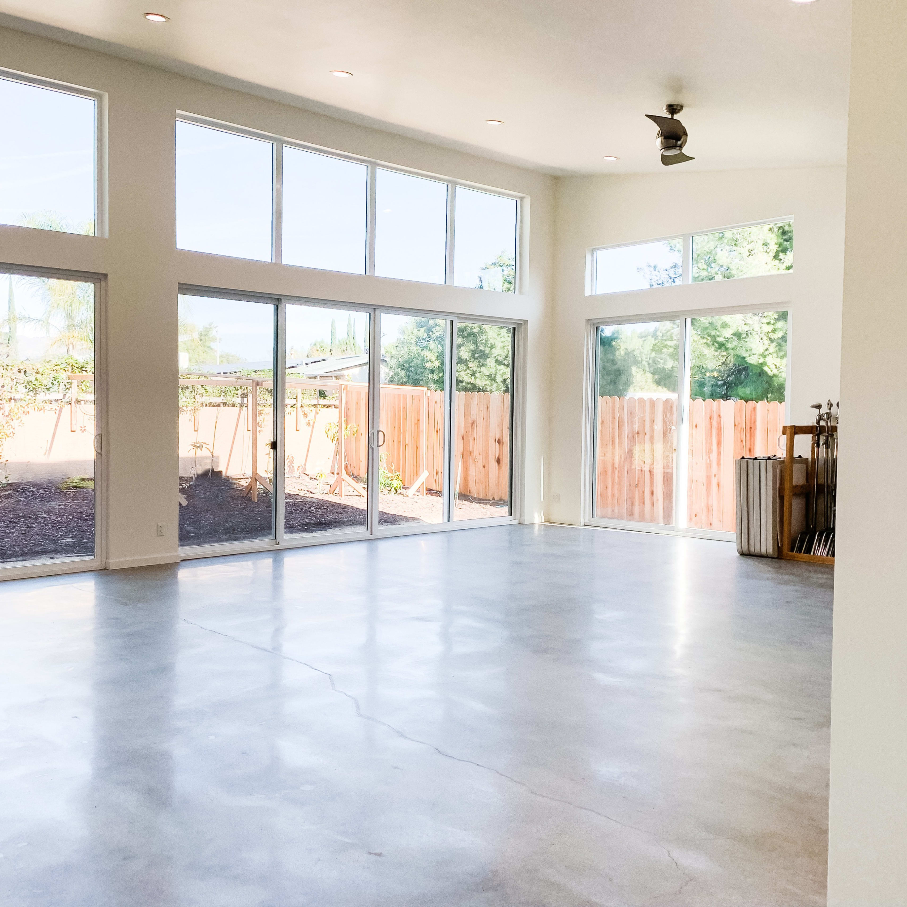 A large, open interior space features concrete flooring and multiple floor-to-ceiling windows that provide ample natural light.