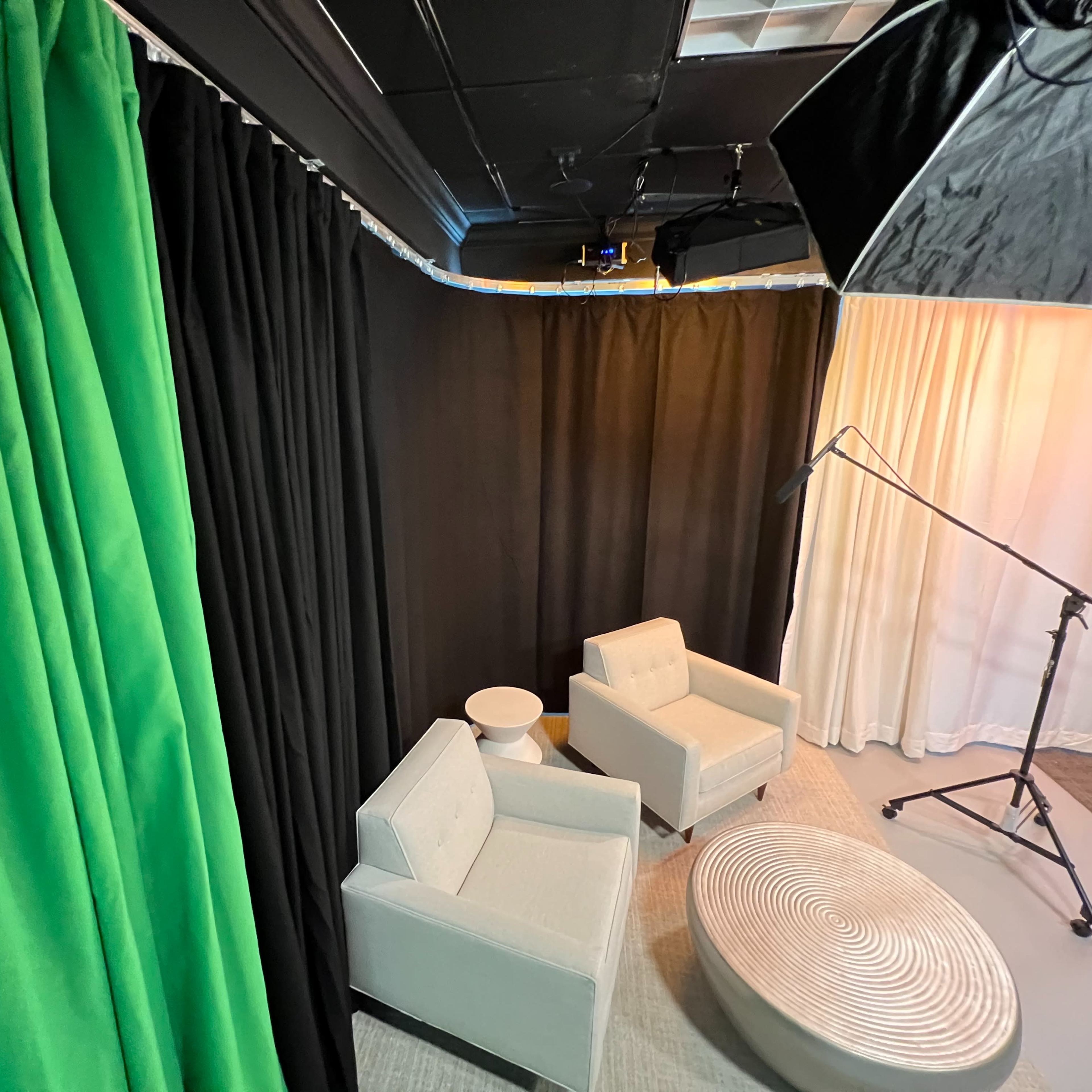 Two light gray chairs positioned near a round white table against a backdrop of green, black, and white curtains in a studio setting.