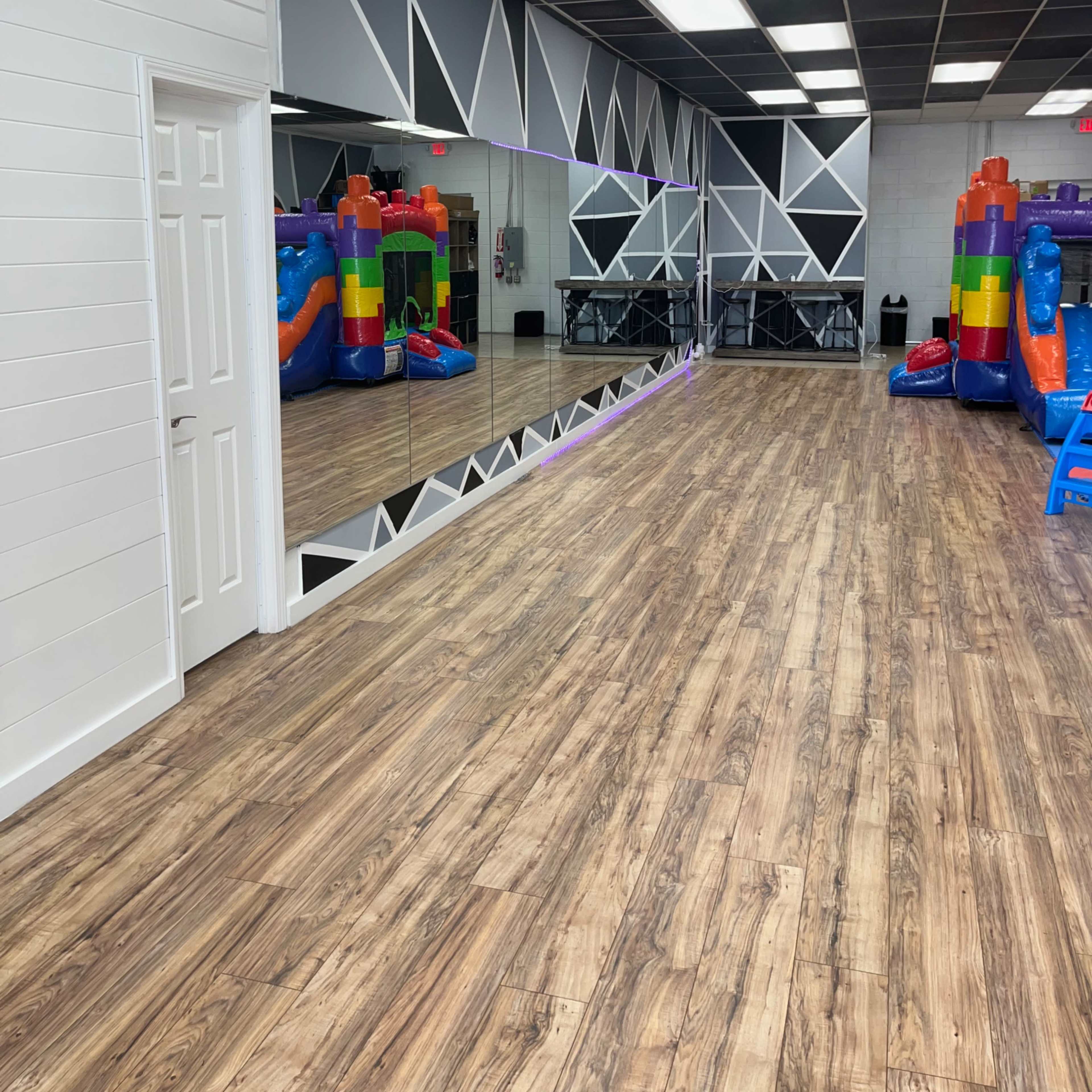 A spacious indoor area with wooden flooring, featuring a large mirror on one wall and inflatable play structures in vibrant colors on the right side.