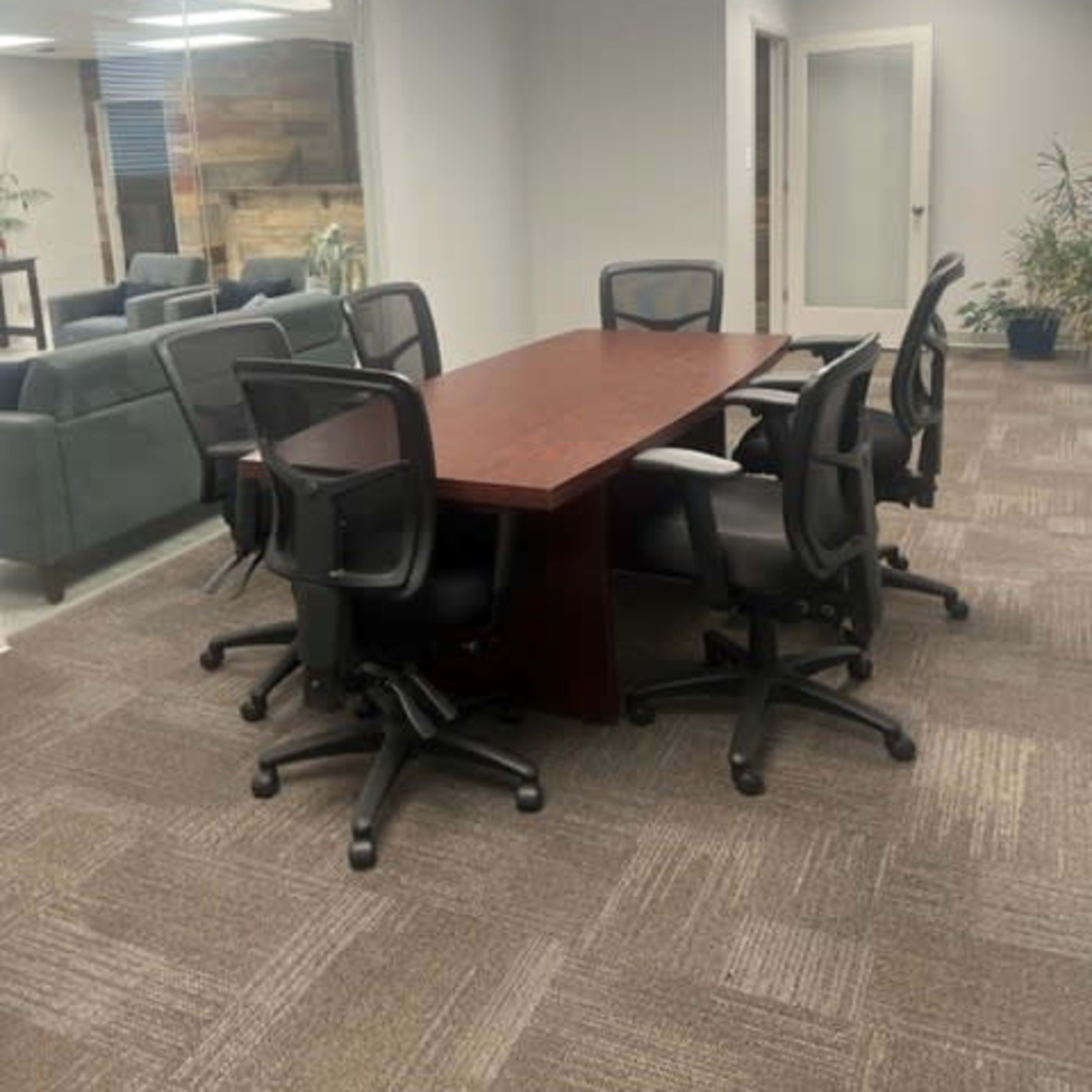 A conference room features a rectangular wooden table surrounded by six black rolling chairs.