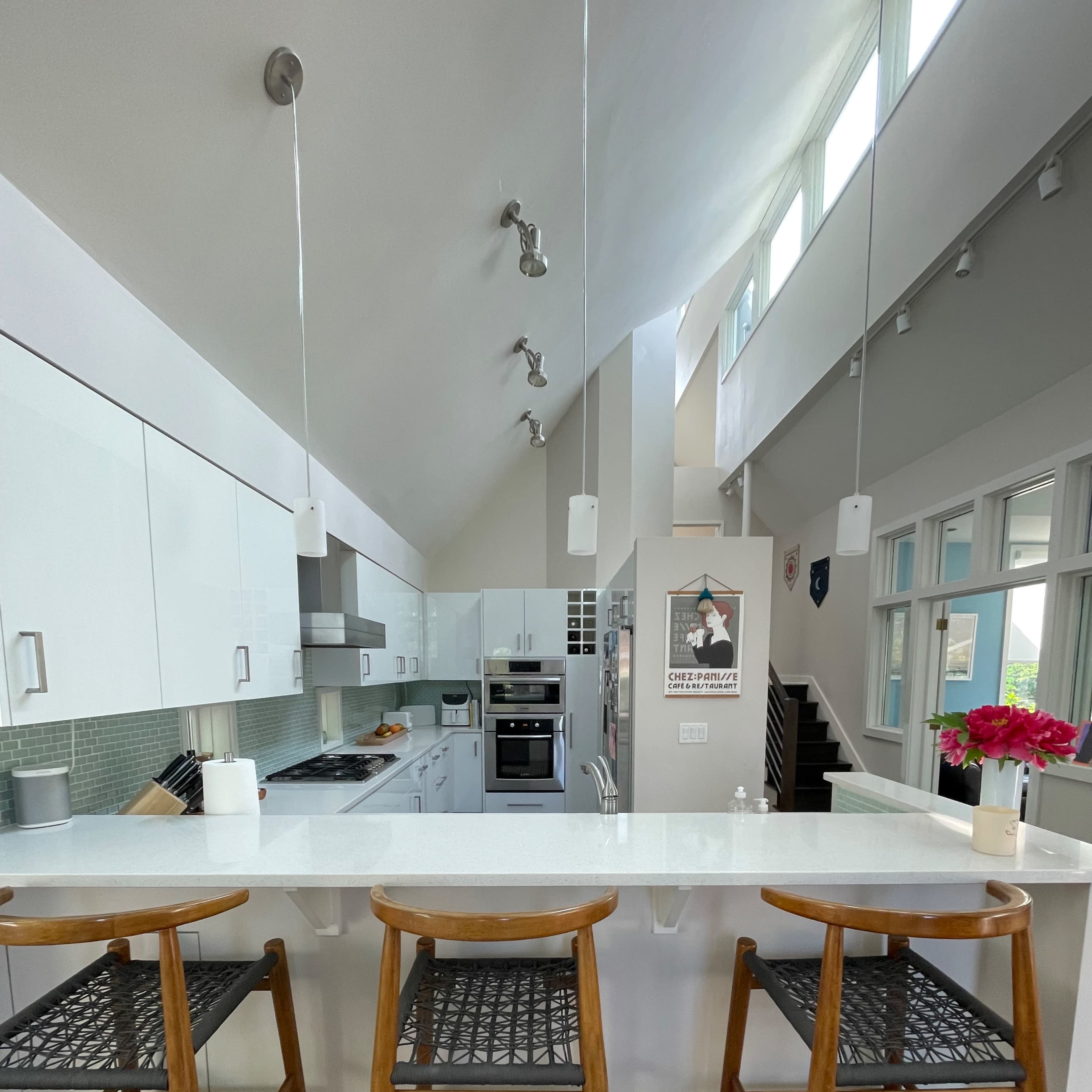 A modern kitchen with white cabinetry, stainless steel appliances, and three wooden bar stools arranged at a counter.