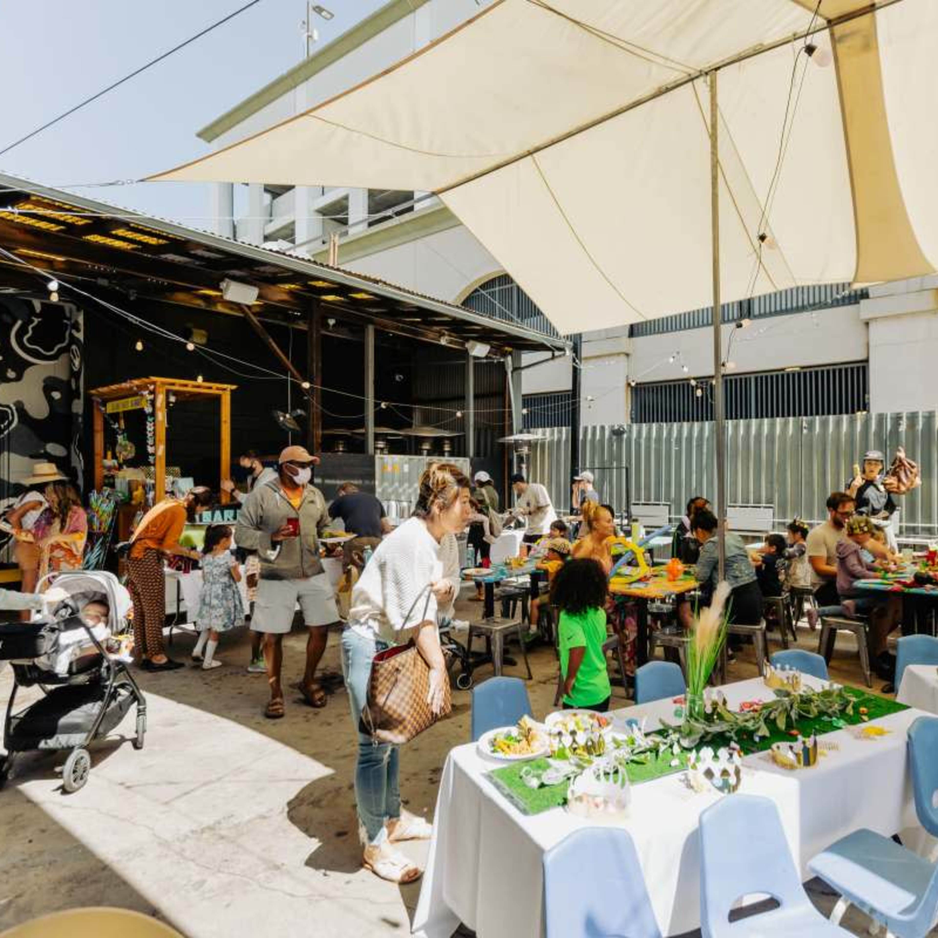 A crowd of people enjoys a lively outdoor gathering under a large canopy, with tables decorated for a celebration.