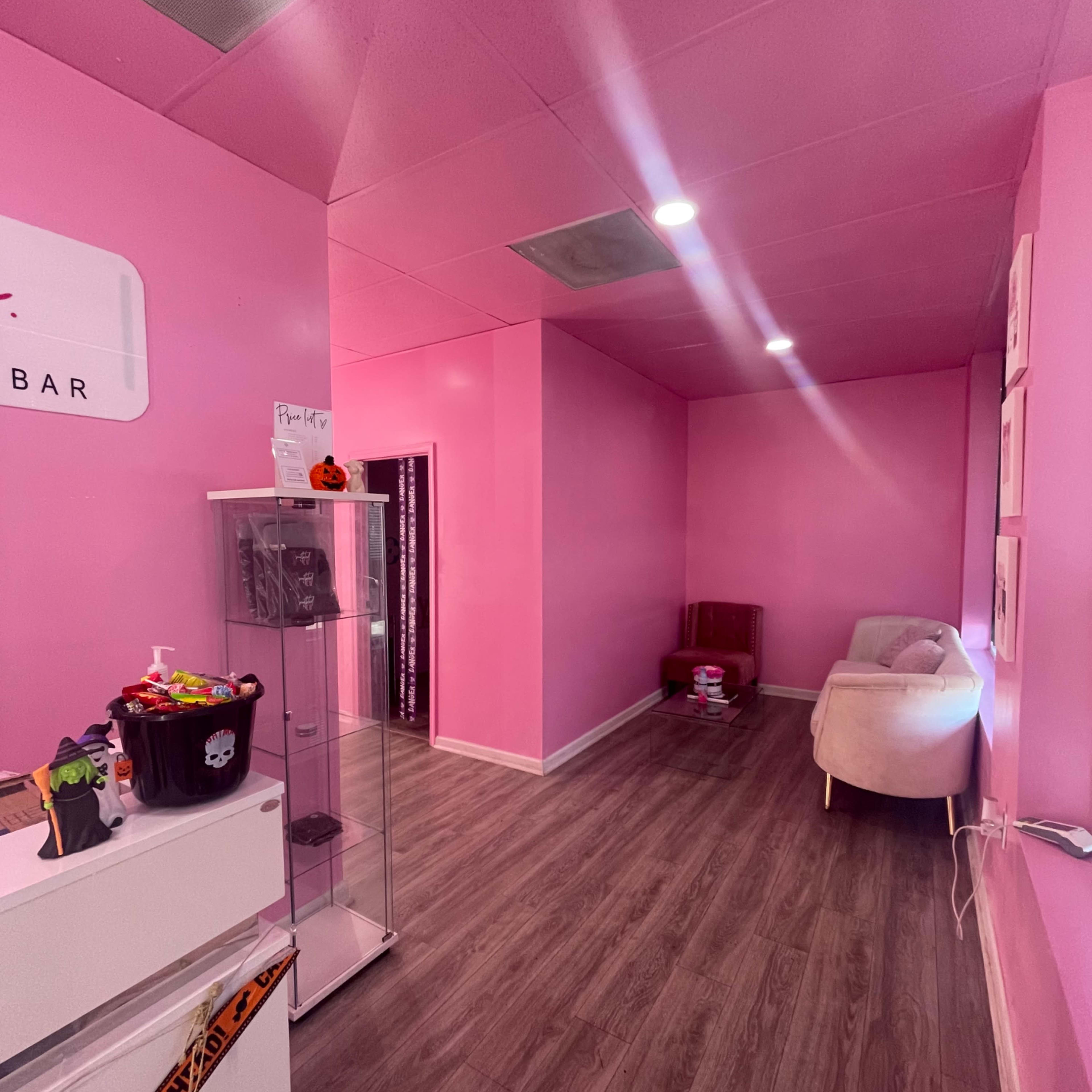 A room with pink walls, wooden flooring, a small seating area, and a display case on the left side.