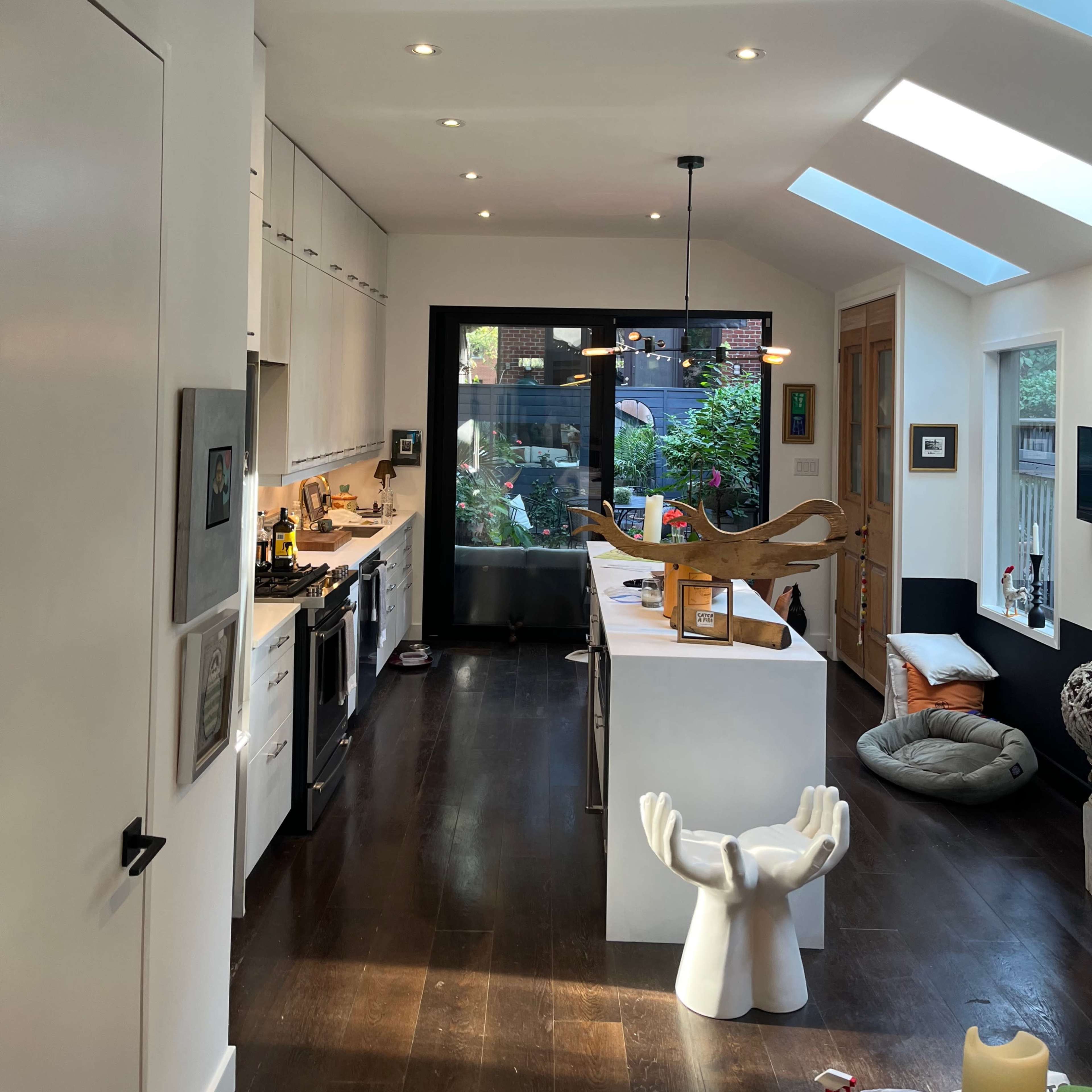 A modern kitchen features white cabinetry, a central island, and large windows overlooking a garden.
