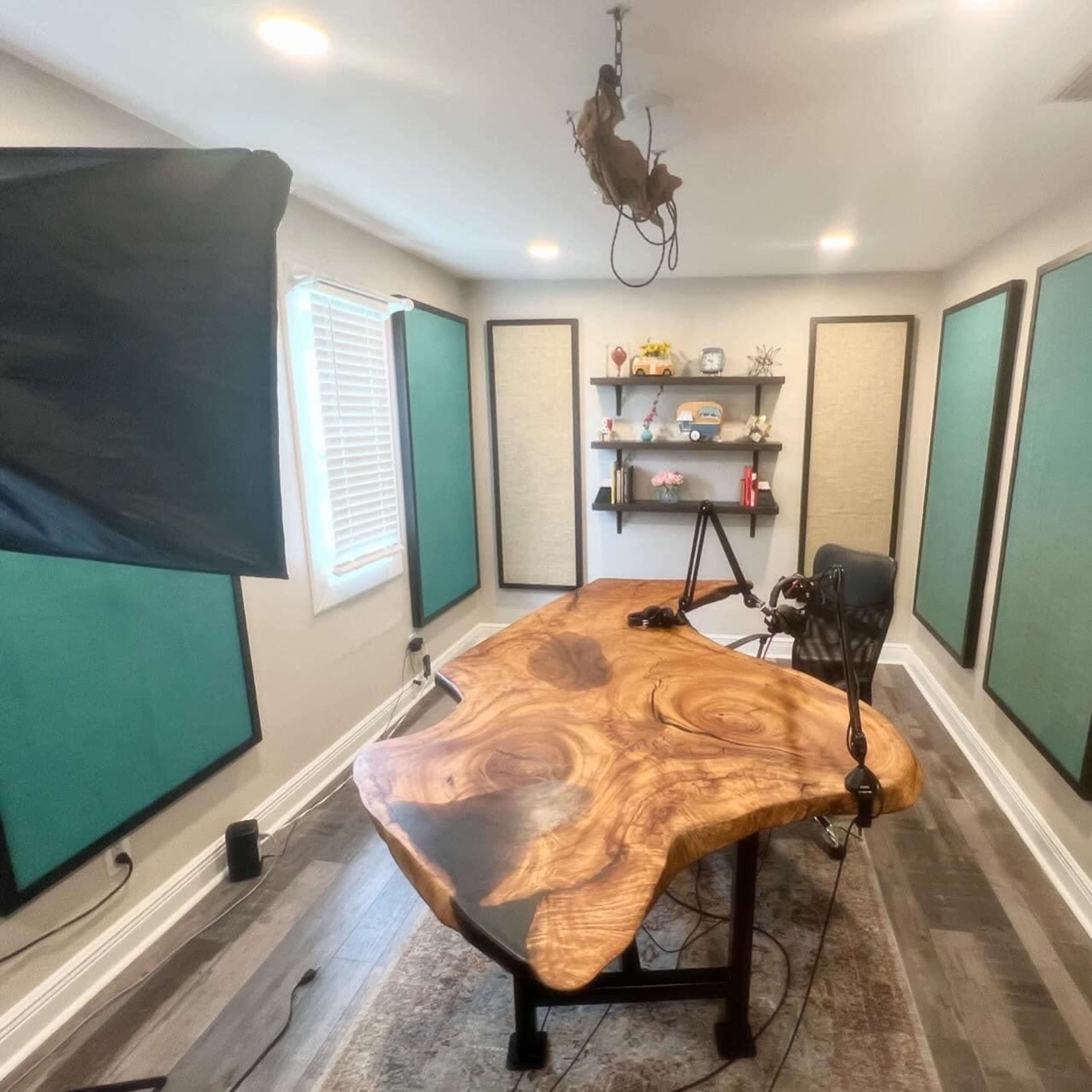 A modern recording studio featuring a large, natural wood table, a microphone setup, and acoustic panels on the walls.