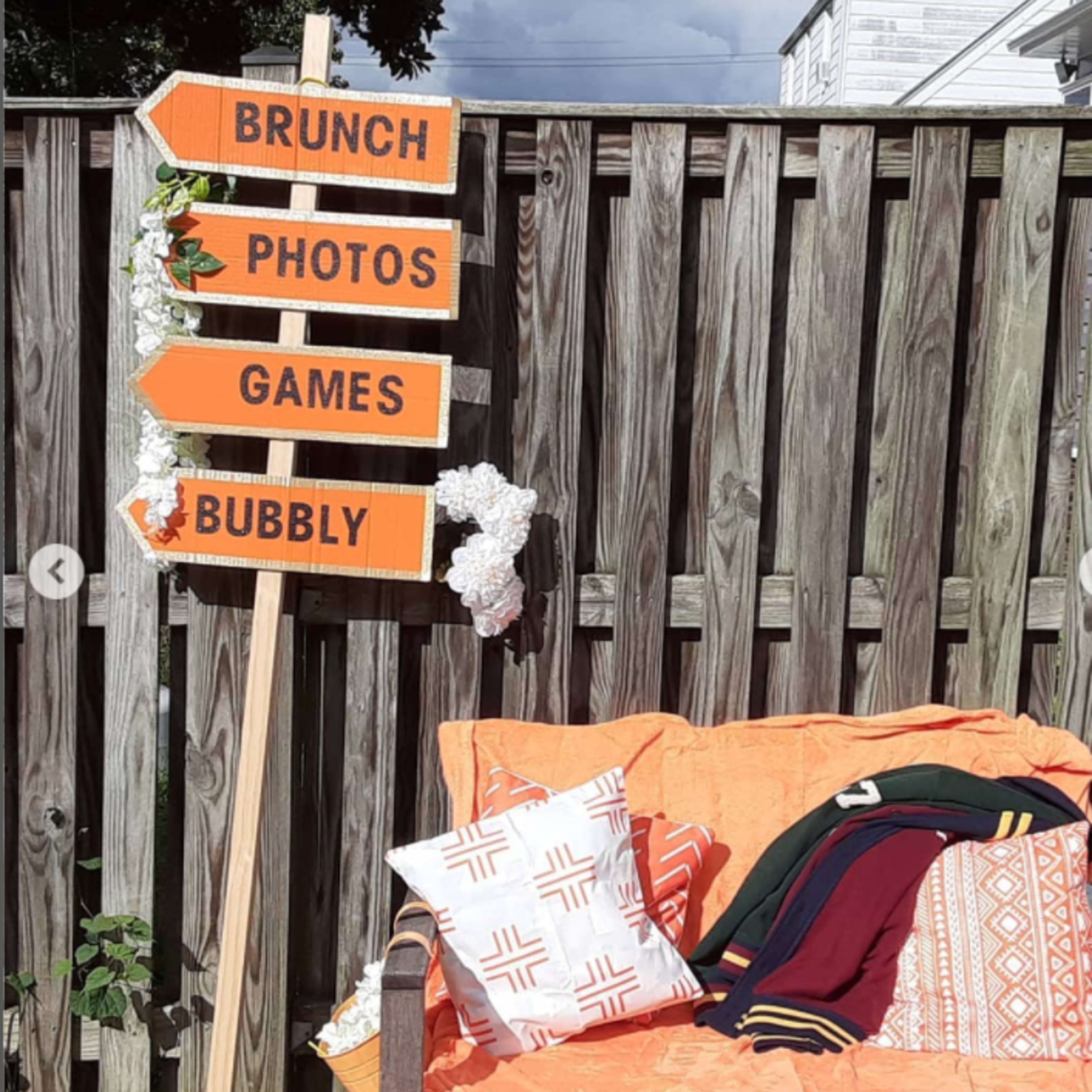 A wooden sign with orange arrows points to different activities, while an orange couch adorned with patterned pillows sits against a wooden fence.