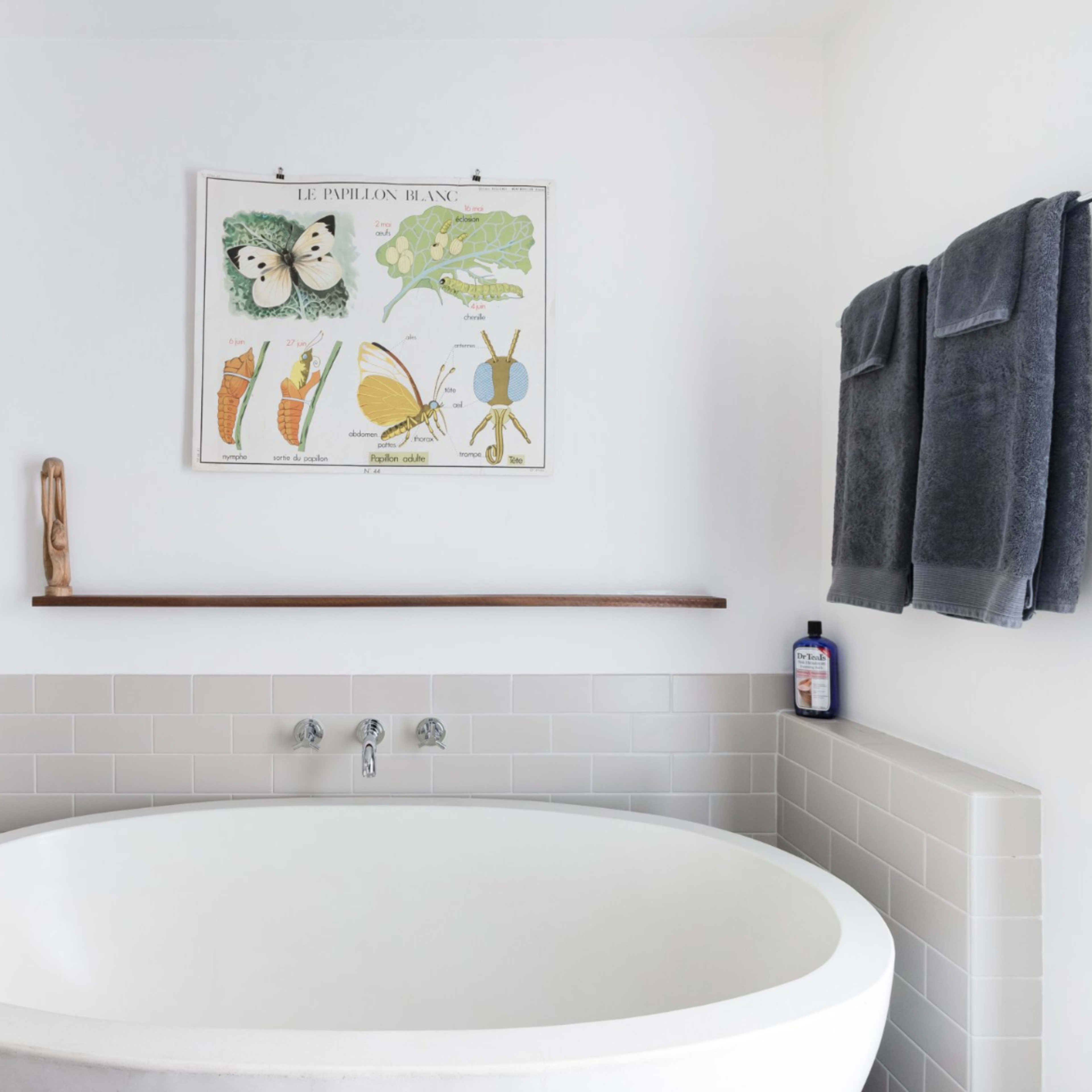 A modern bathroom with a curved bathtub, a shower area, and a wall-mounted art print above a wooden shelf.